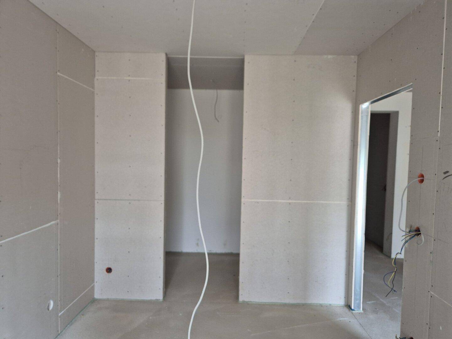 Raum im Rohbau mit Gipskartonwänden und sichtbaren Kabeln, bereit für den weiteren Ausbau.
