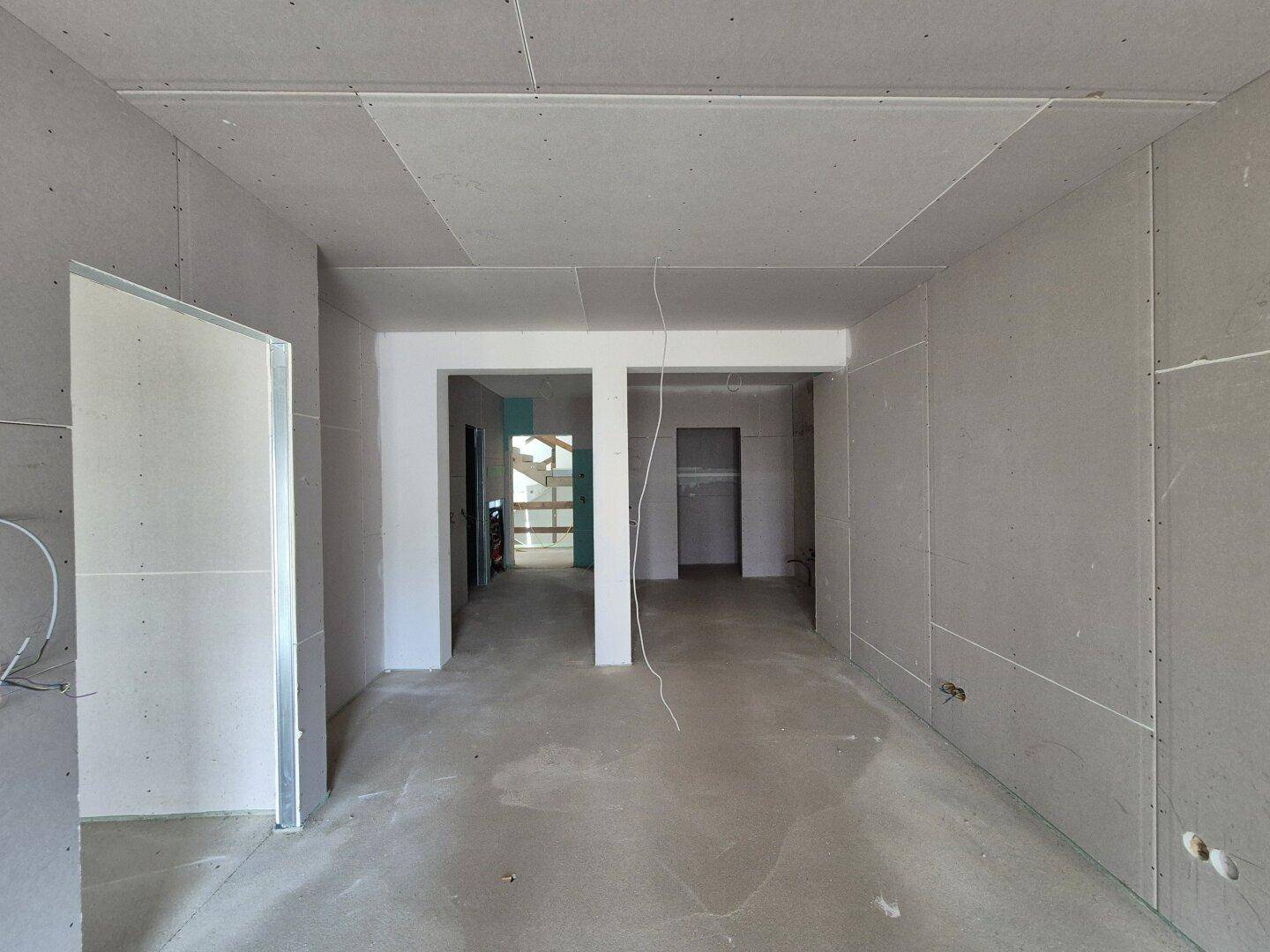 Großer Raum im Rohbau mit Gipskartonwänden und offenem Durchgang, bereit für den Innenausbau.
