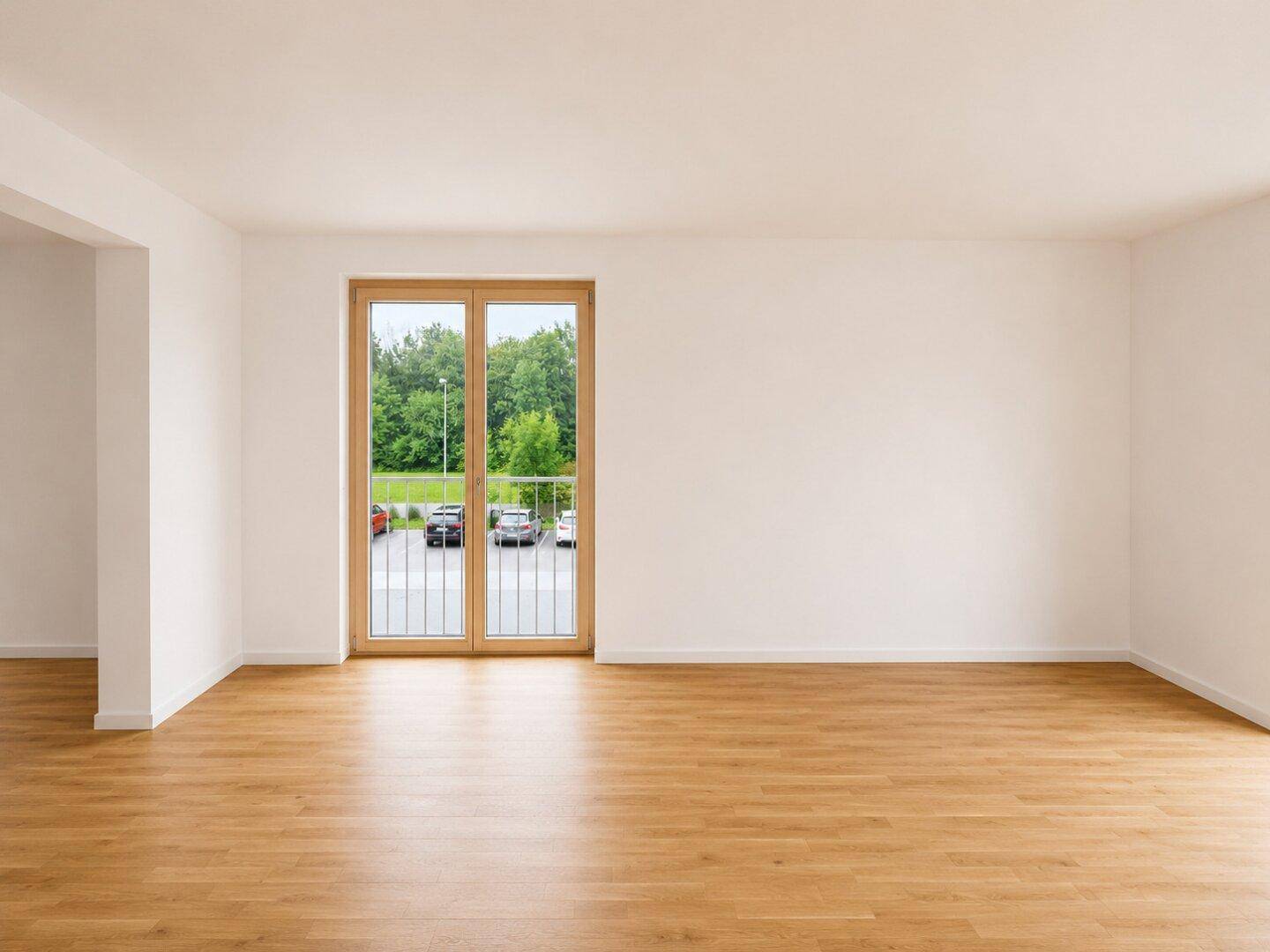 Geräumiger, heller Raum mit Holzboden und Balkontür, die den Blick ins Grüne freigibt.