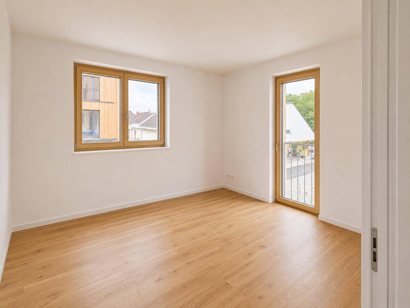 Lichtdurchflutetes Zimmer mit Holzboden, Fenster und Balkontür, ideal als Schlafzimmer.