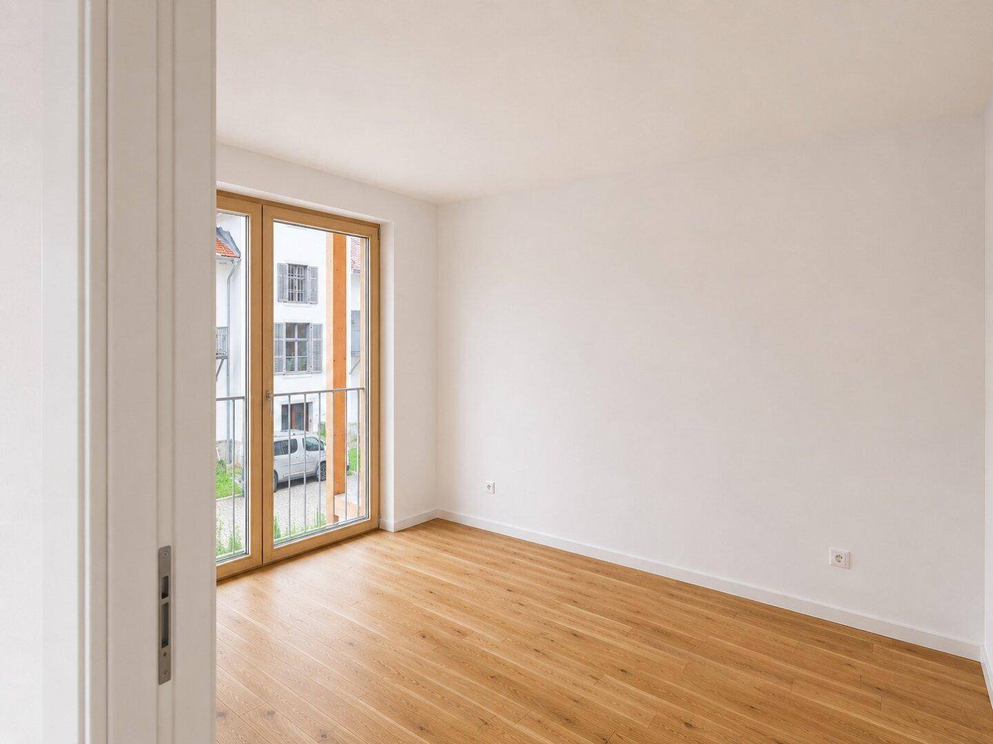 Helles Schlafzimmer mit Holzboden und Zugang zu einem französischen Balkon.