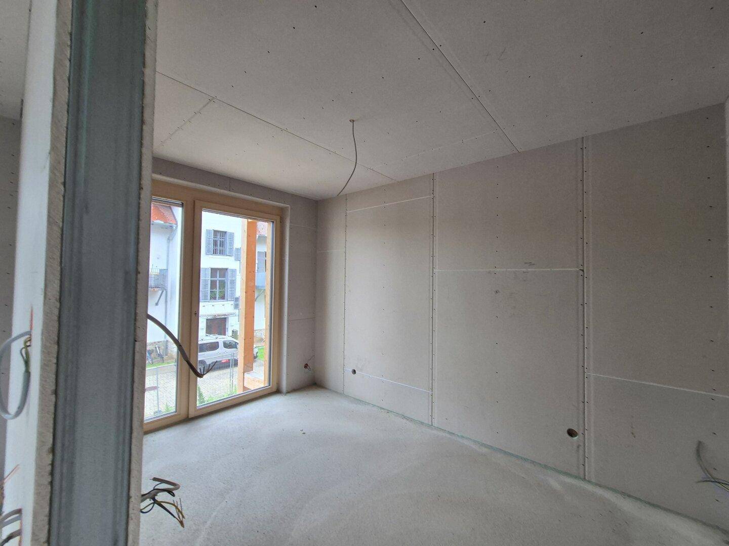 Rohbau eines Schlafzimmers mit Betonboden und Zugang zu einem französischen Balkon.