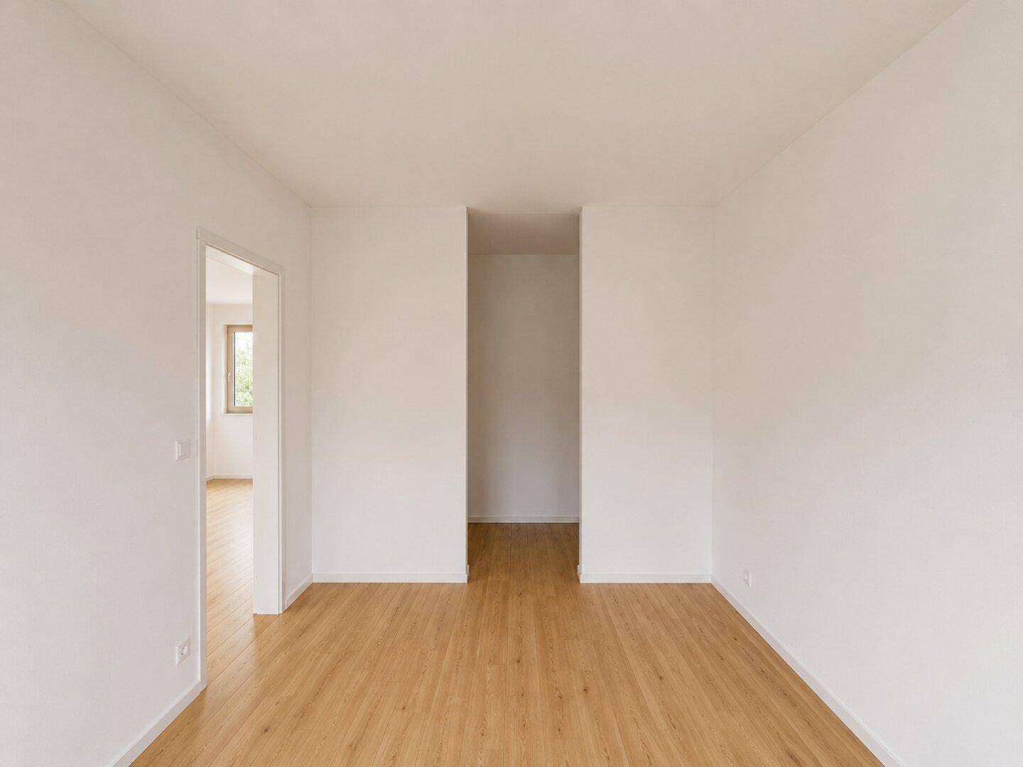 Leerer Innenraum im Rohbau mit hellem Laminatboden und weiß gestrichenen Wänden.