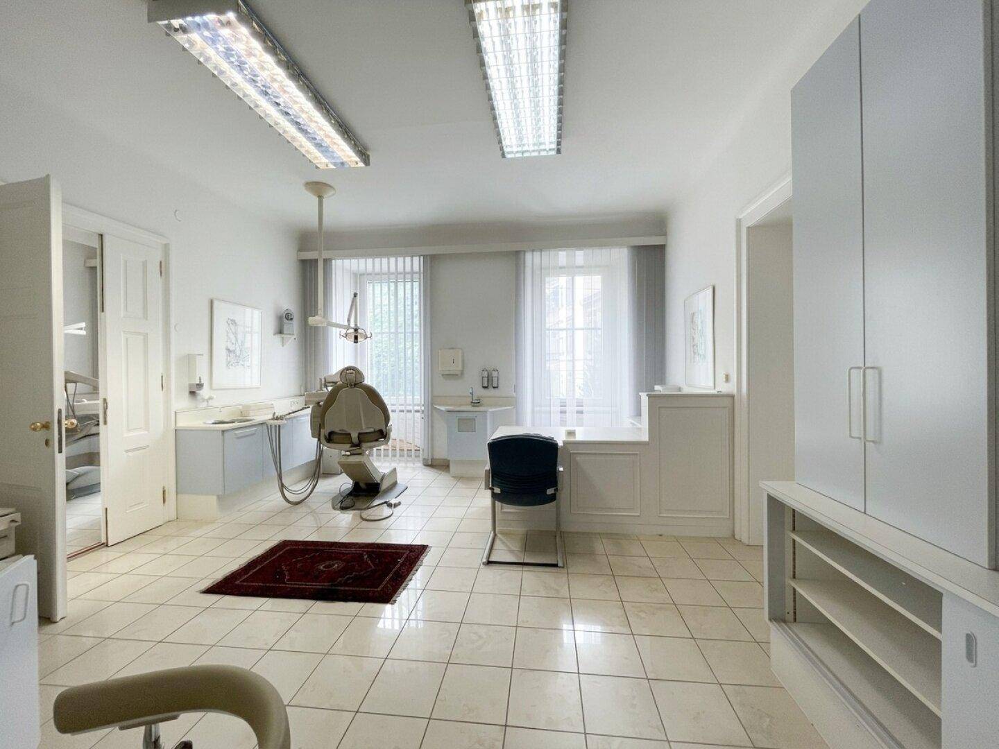 Geräumiger Behandlungsraum mit Fliesenboden, medizinischen Geräten und großen Fenstern für viel Licht.
