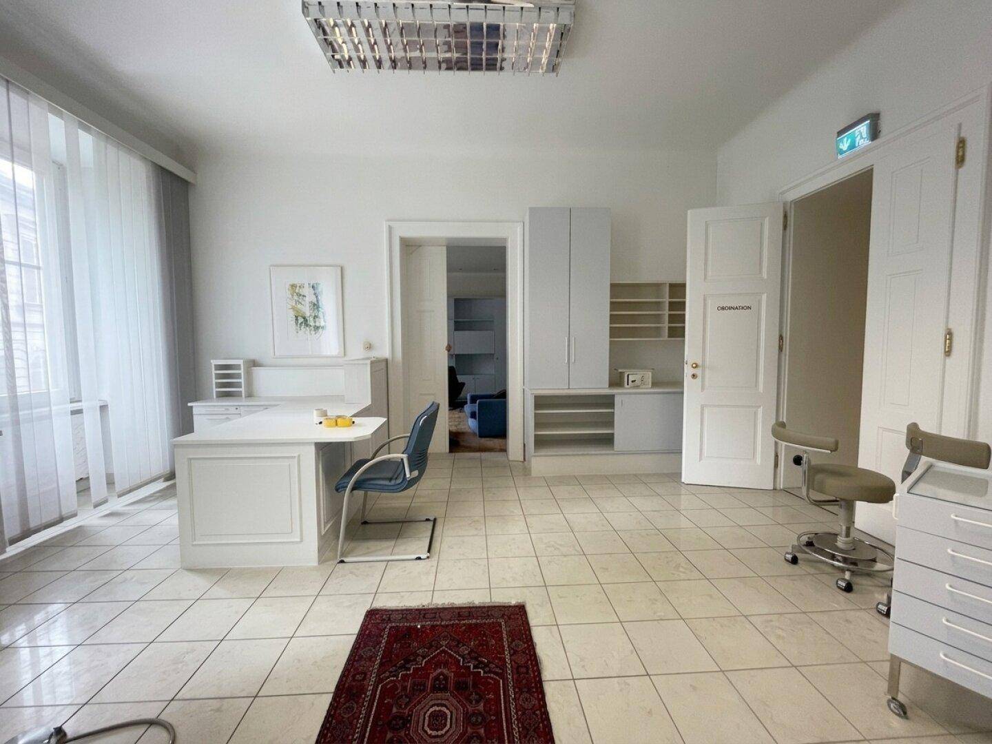 Heller Büroraum mit Fliesenboden, Schreibtisch und Stauraum, bereit für professionelle Nutzung.