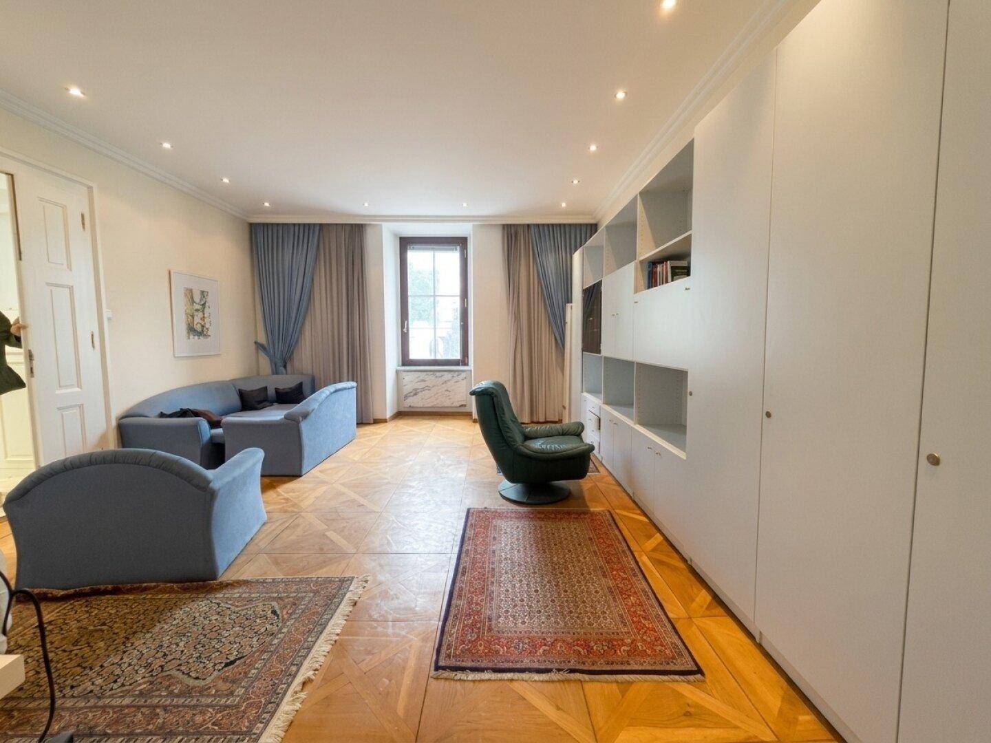 Geräumiges Büro mit elegantem Parkettboden, Einbauschränken und bequemen Sitzmöbeln in Blautönen.