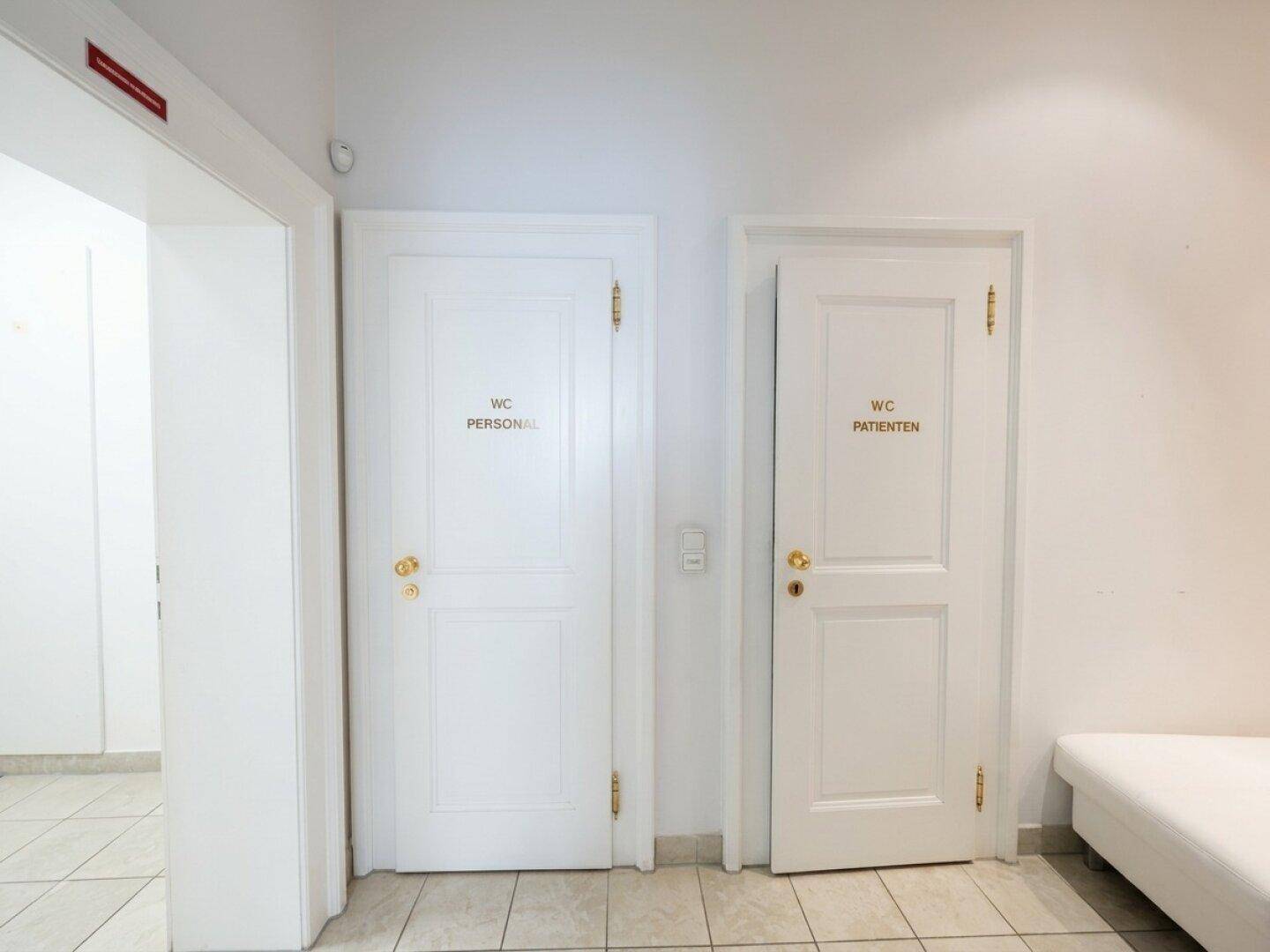 Flur mit zwei weißen Türen, die zu den Toiletten für Personal und Patienten führen.