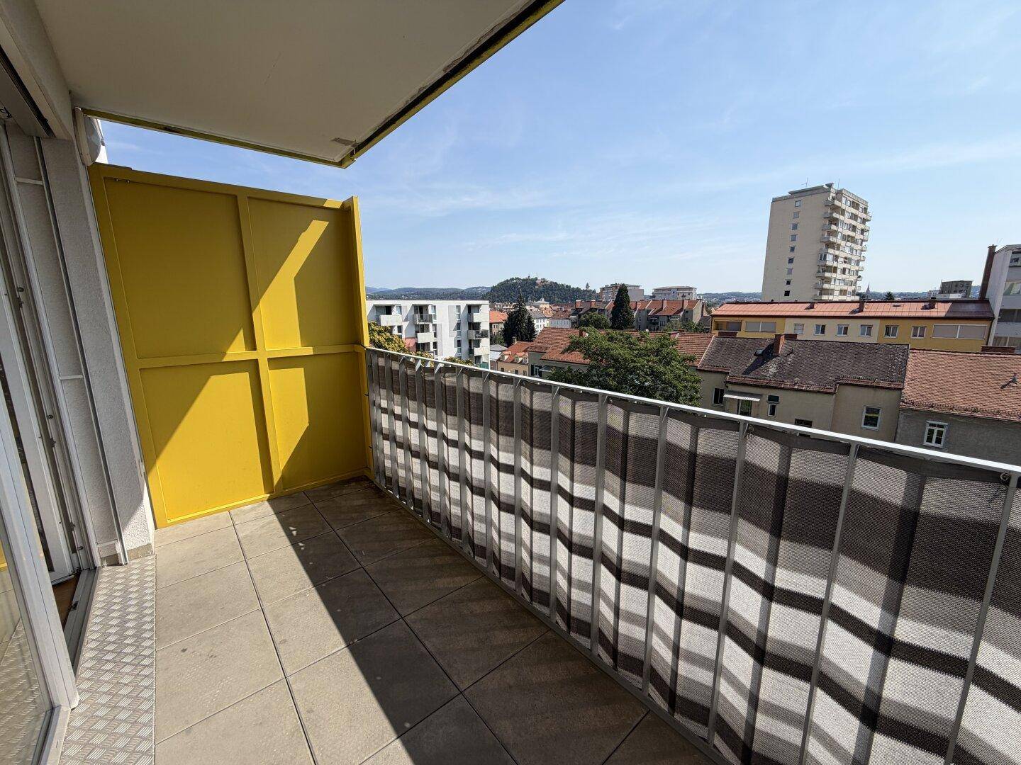 Sonniger Balkon mit Stadtblick und gelbem Sichtschutz, ideal für entspannte Stunden im Freien.