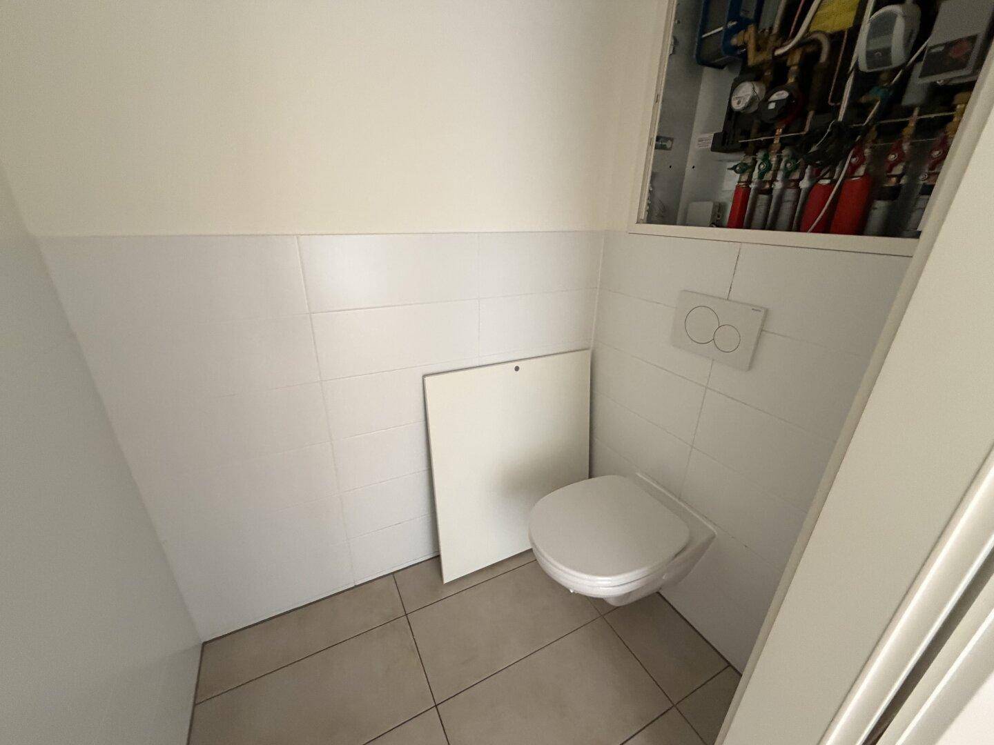 Separates WC mit wandhängender Toilette und weißen Fliesen, funktional und sauber.