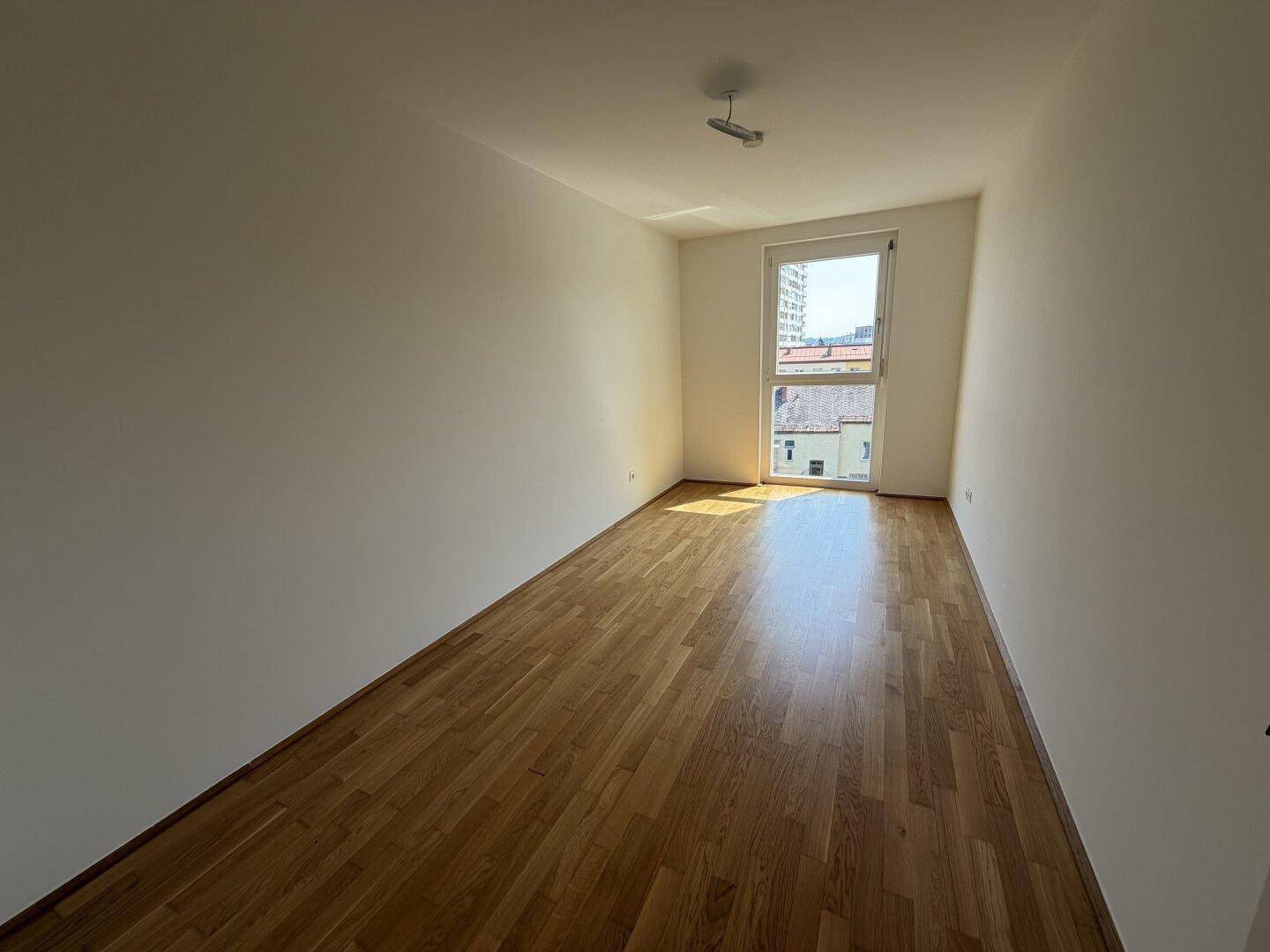 Geräumiges Schlafzimmer mit Holzboden und Fenster, das einen Blick auf die Umgebung bietet.