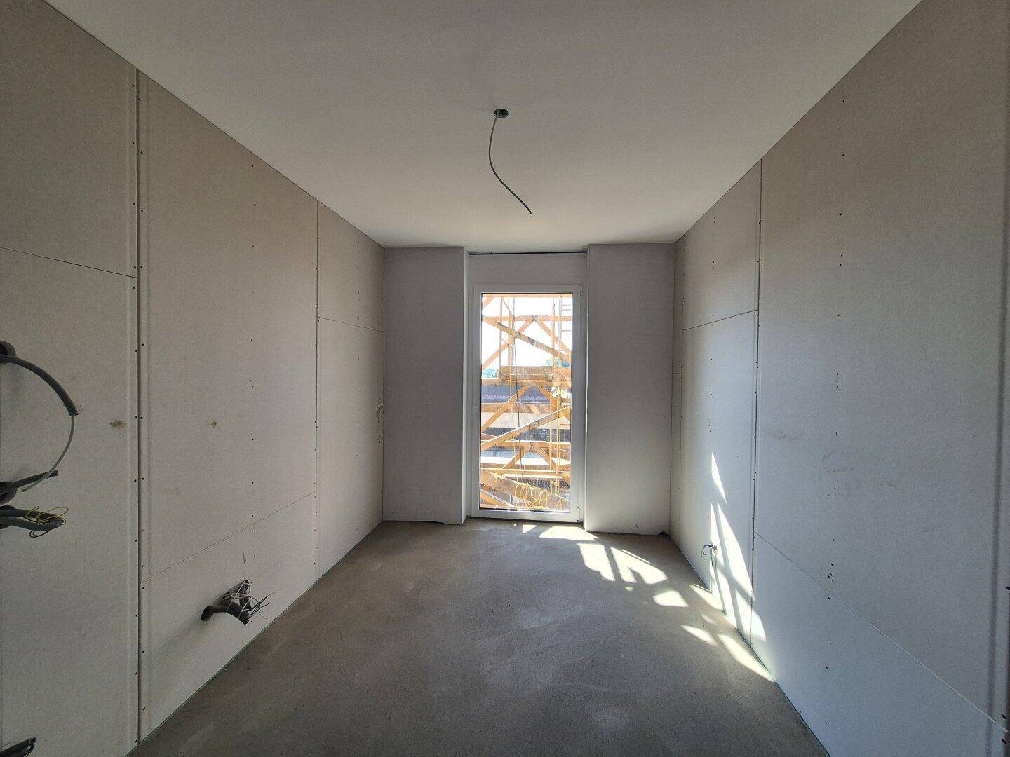 Zimmer im Rohbauzustand mit Trockenbauwänden und Betonboden, Blick auf die Baustelle.