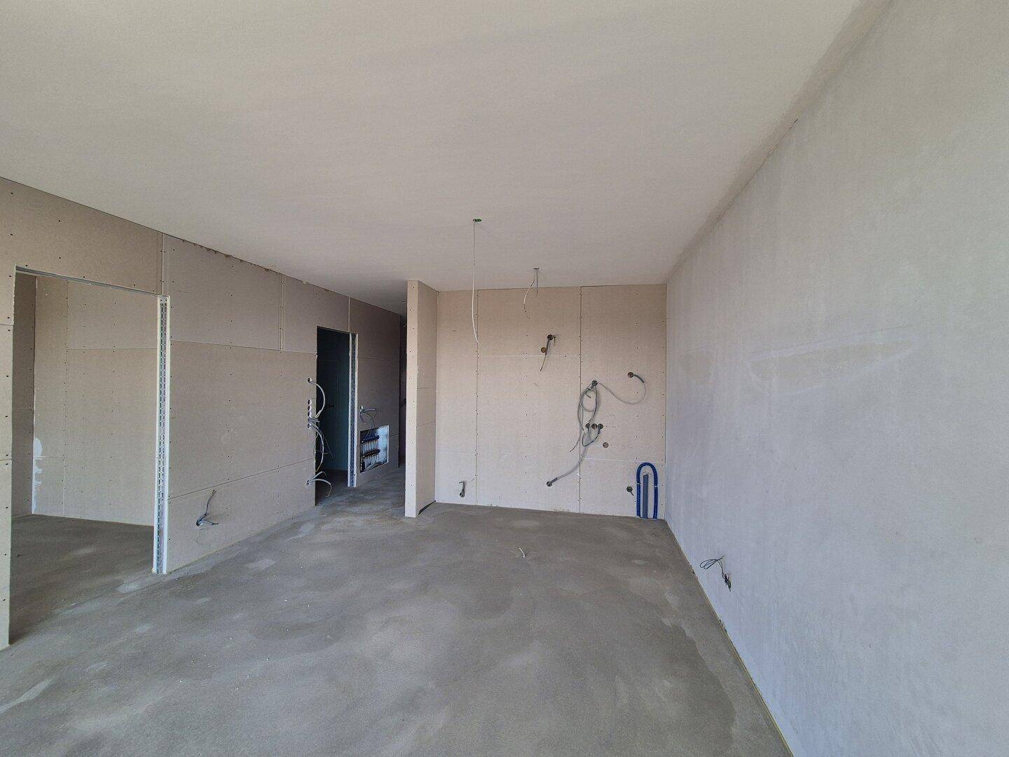 Großer unfertiger Raum mit Betonboden und vorbereiteten Installationen für Elektrik und Sanitär.