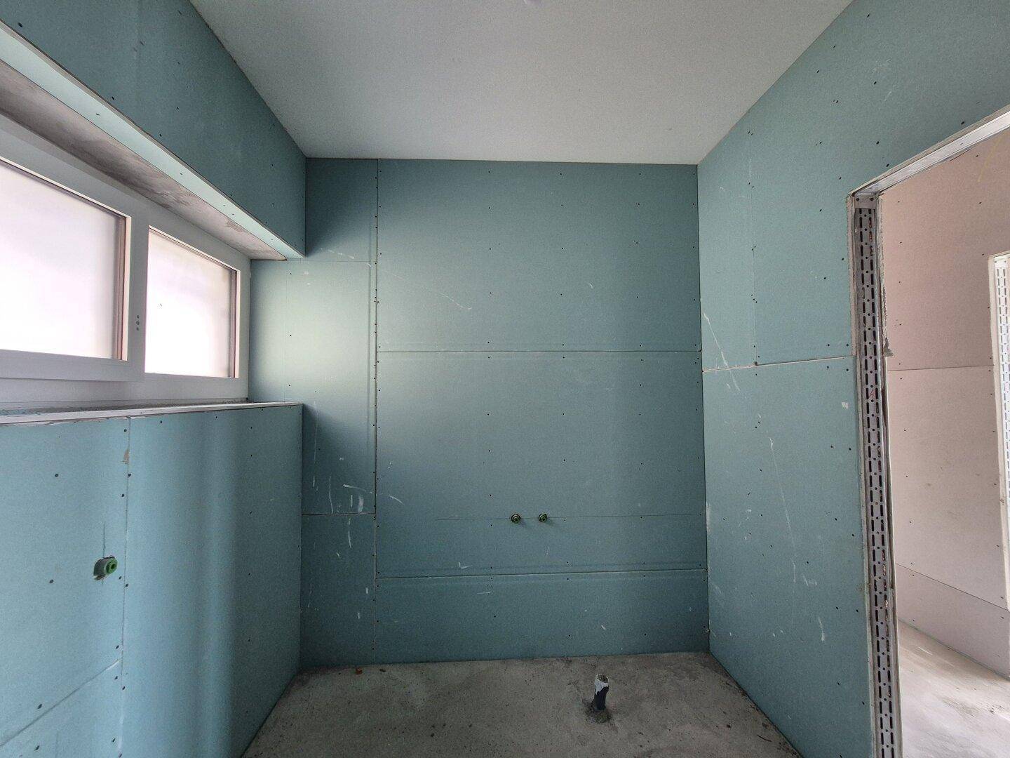 Badezimmer im Rohbau mit blauen Gipskartonplatten und vorbereiteten Anschlüssen für Sanitärinstallationen.