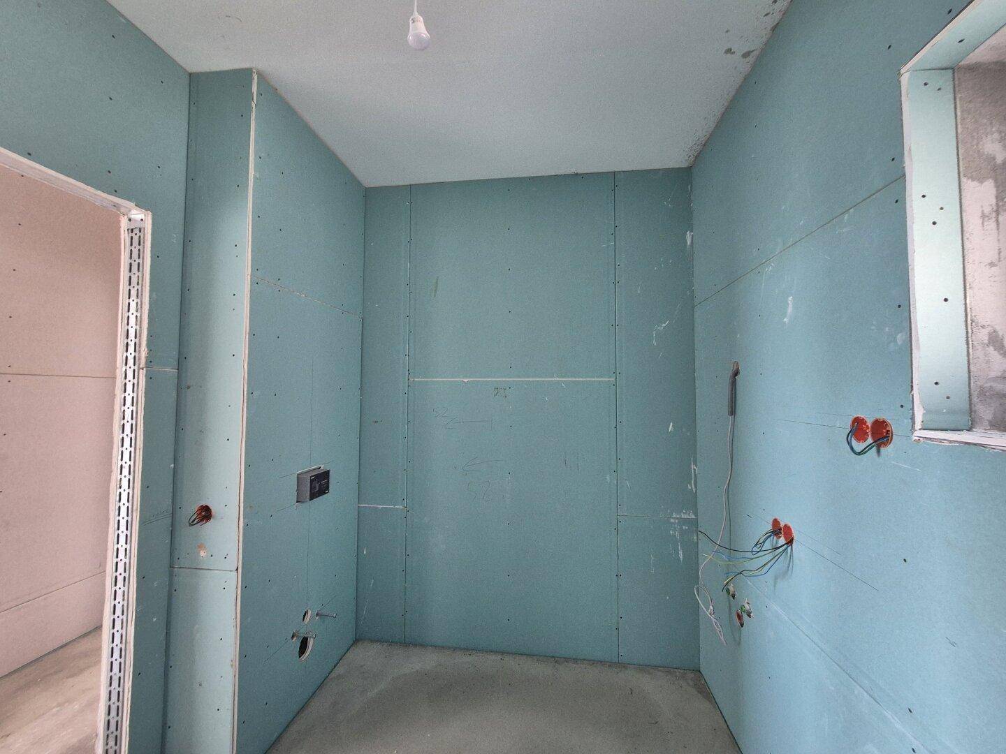 Badezimmer im Rohbau mit blauen Gipskartonplatten und vorbereiteten Anschlüssen für Sanitärinstallationen.