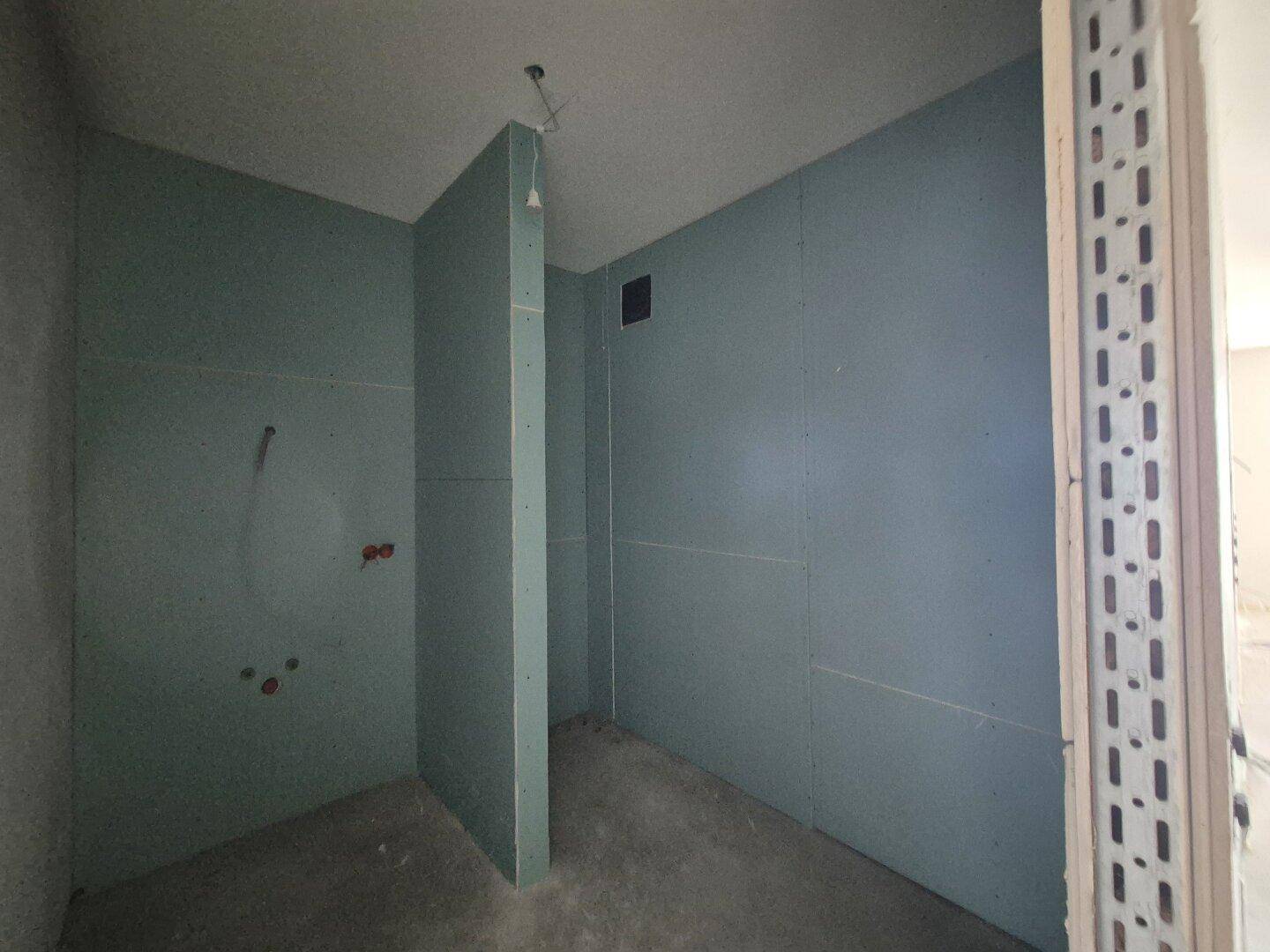 Unfertiges Badezimmer mit feuchtigkeitsbeständigen Trockenbauwänden, bereit für die Installation der Sanitäreinrichtungen.