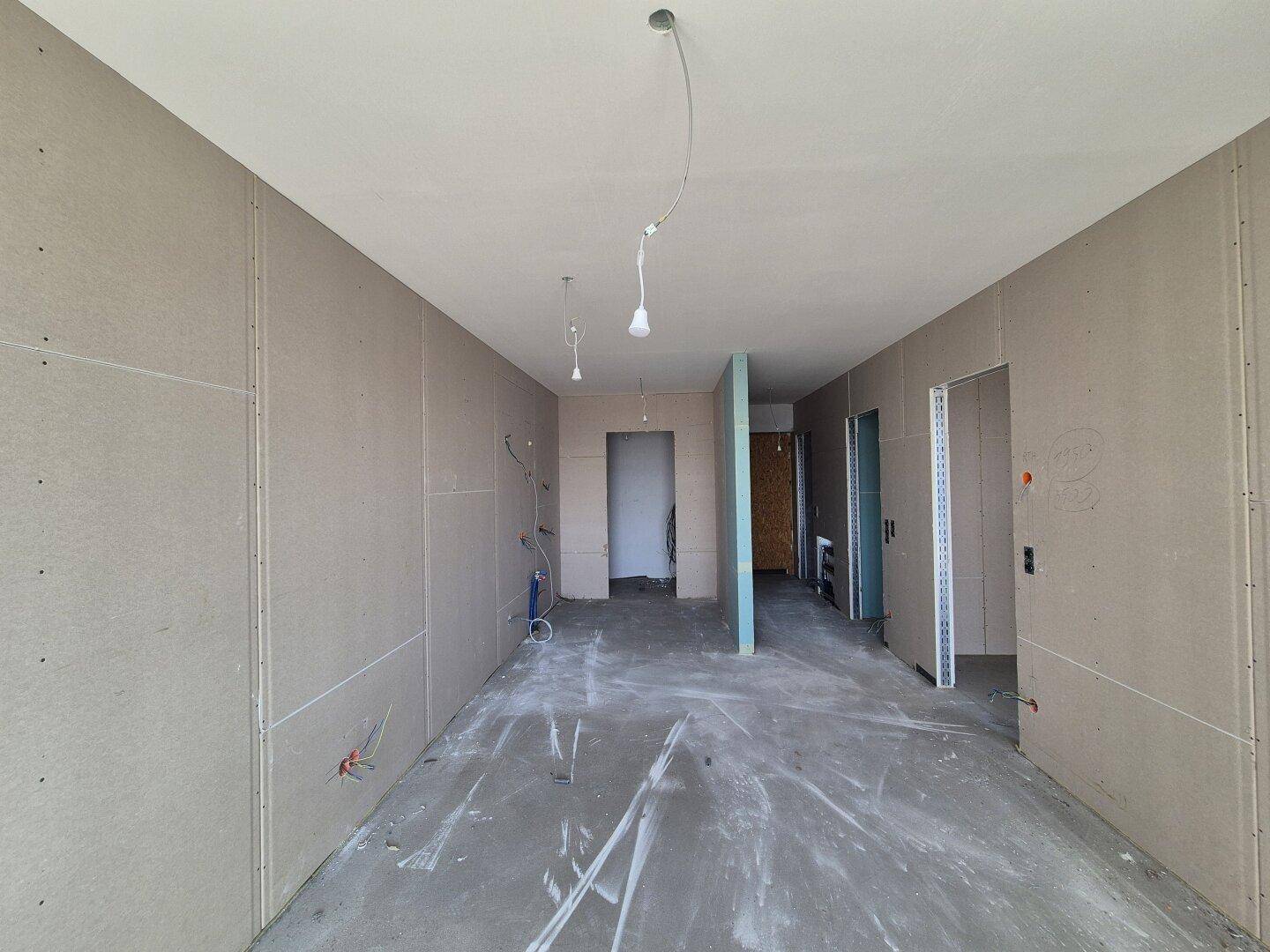 Großer, unfertiger Innenraum mit Trockenbauwänden und Betonboden, der den Baufortschritt zeigt.