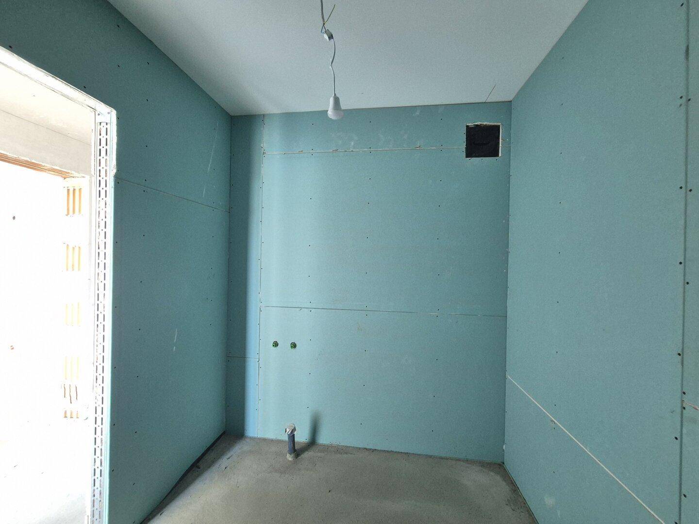 Badezimmer im Rohbau mit blauen Trockenbauwänden und sichtbaren Wasseranschlüssen.