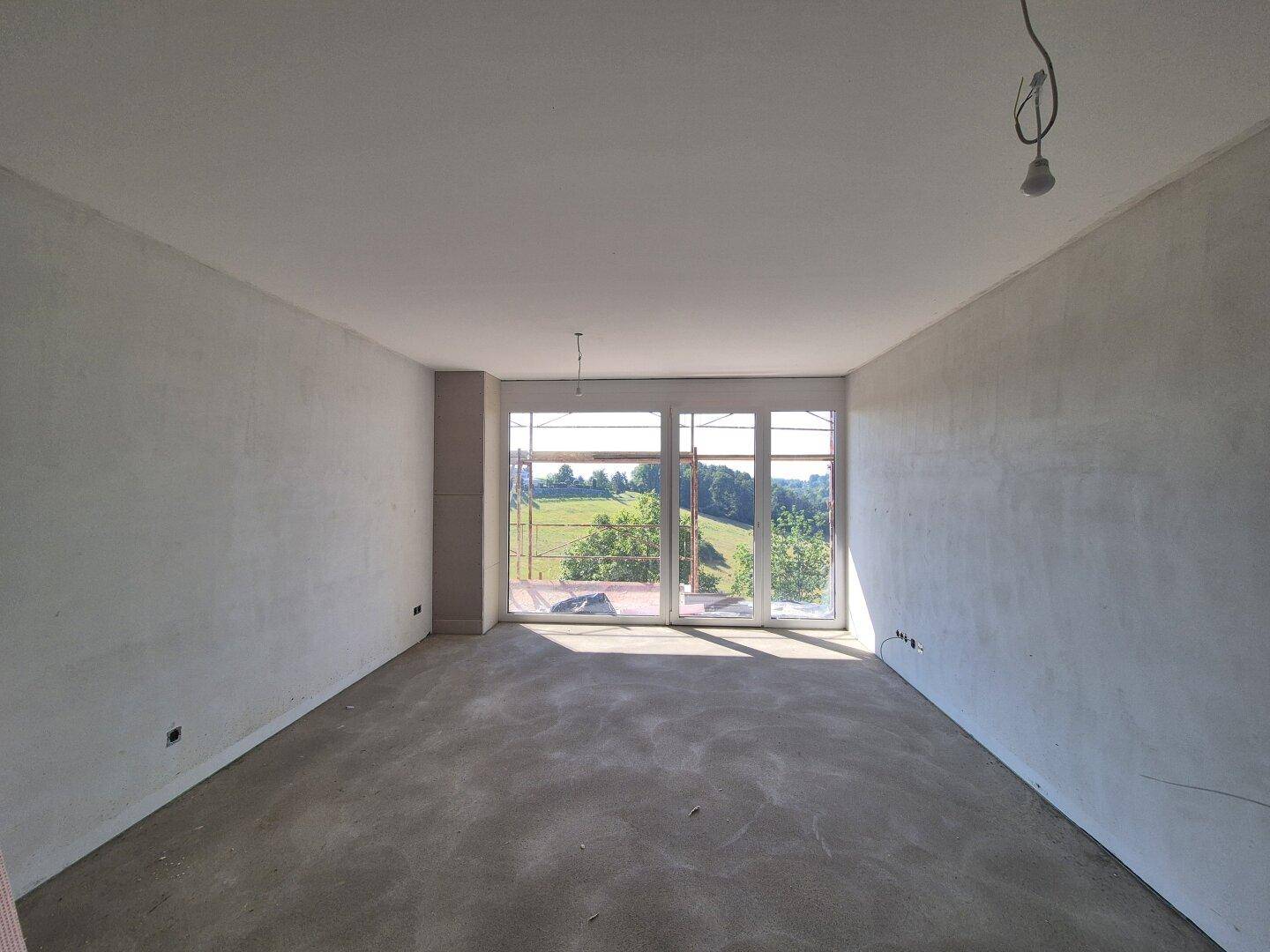 Geräumiger Rohbau mit Betonboden und großen Fenstern, die einen weiten Blick auf die Landschaft ermöglichen.