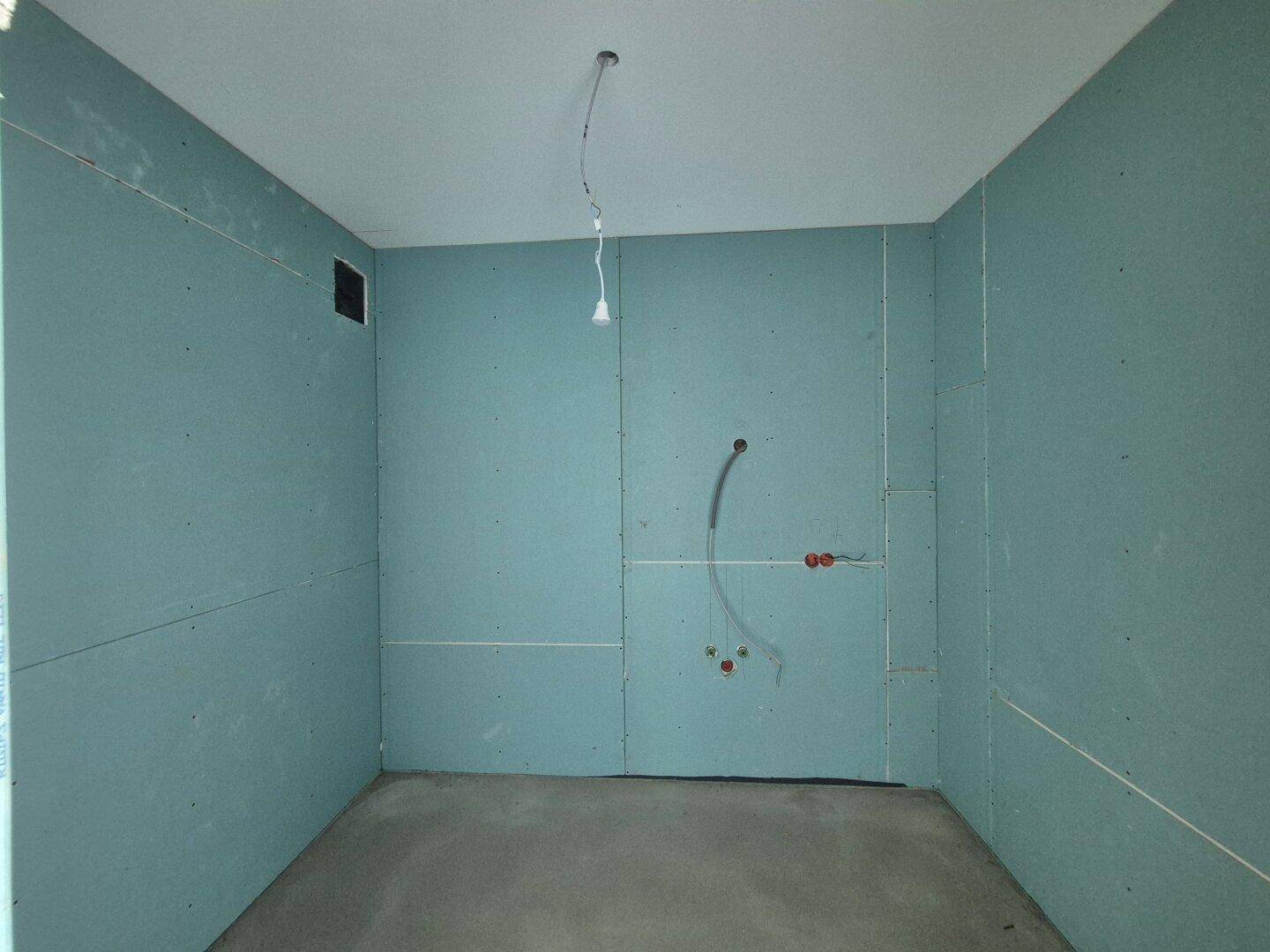 Badezimmer im Rohbau mit blauen Trockenbauwänden und vorbereiteten Anschlüssen für Sanitäranlagen.