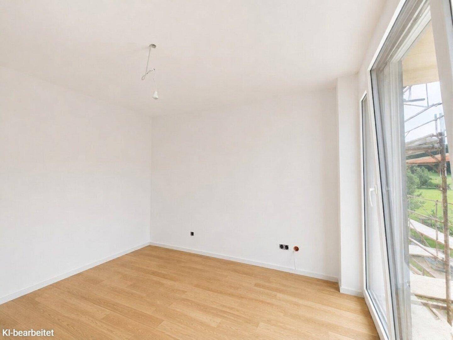 Helles, unmöbliertes Zimmer mit Holzboden und Fenster, das auf eine Baustelle blickt.