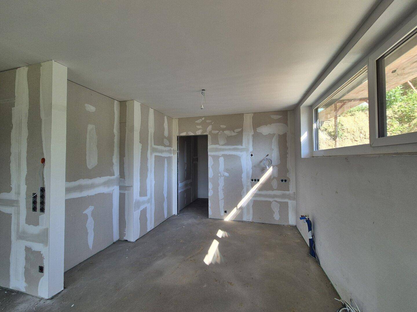 Raum im Rohbau mit Trockenbauwänden, Betonboden und einem Fenster, bereit für den Innenausbau.