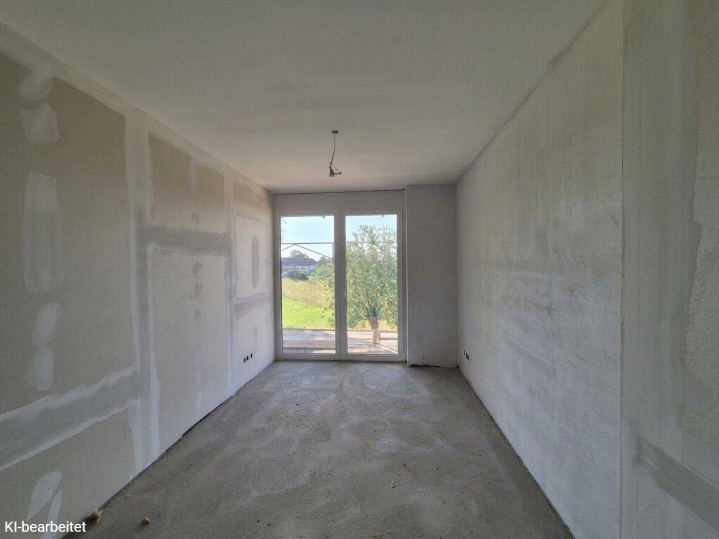 Unfertiger Raum mit Trockenbauwänden und Betonboden, mit großem Fenster und Blick ins Grüne.