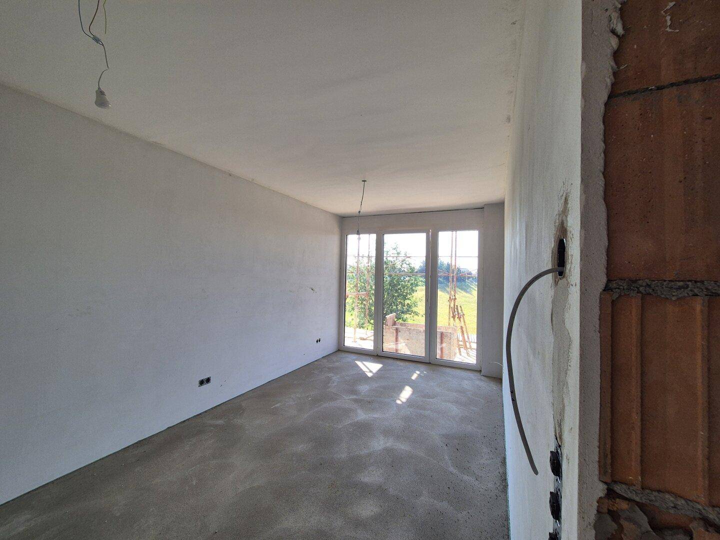 Rohbauzimmer mit großen Fenstern und Blick ins Grüne, noch ohne finalen Bodenbelag.