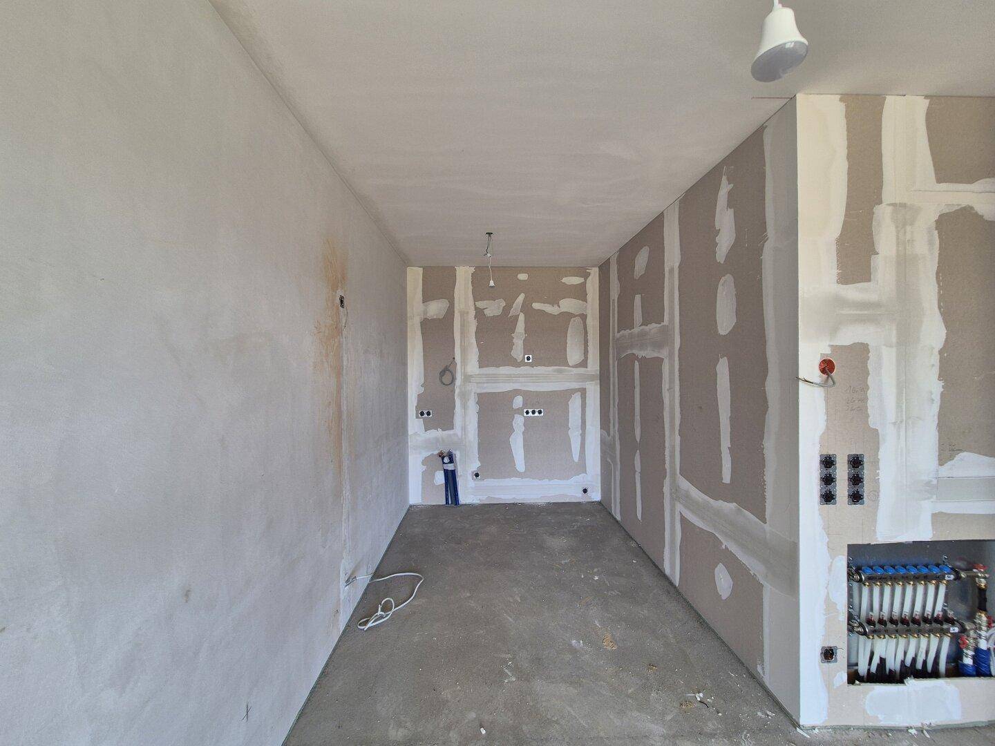 Rohbau einer Küche mit sichtbaren Installationen und unfertigen Wänden, bereit für den Ausbau.