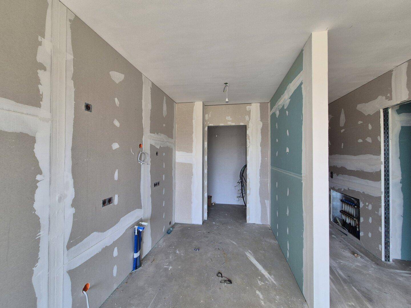 Unfertiger Raum mit Trockenbauwänden, sichtbaren Installationen und Betonboden während der Bauphase.