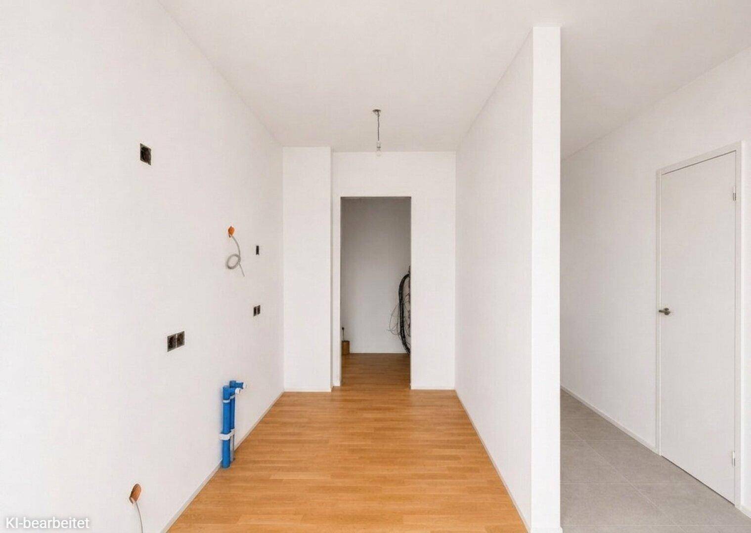 Unfertiger Flur mit Holzboden, sichtbaren Installationen und Zugang zu weiteren Räumen im Neubau.