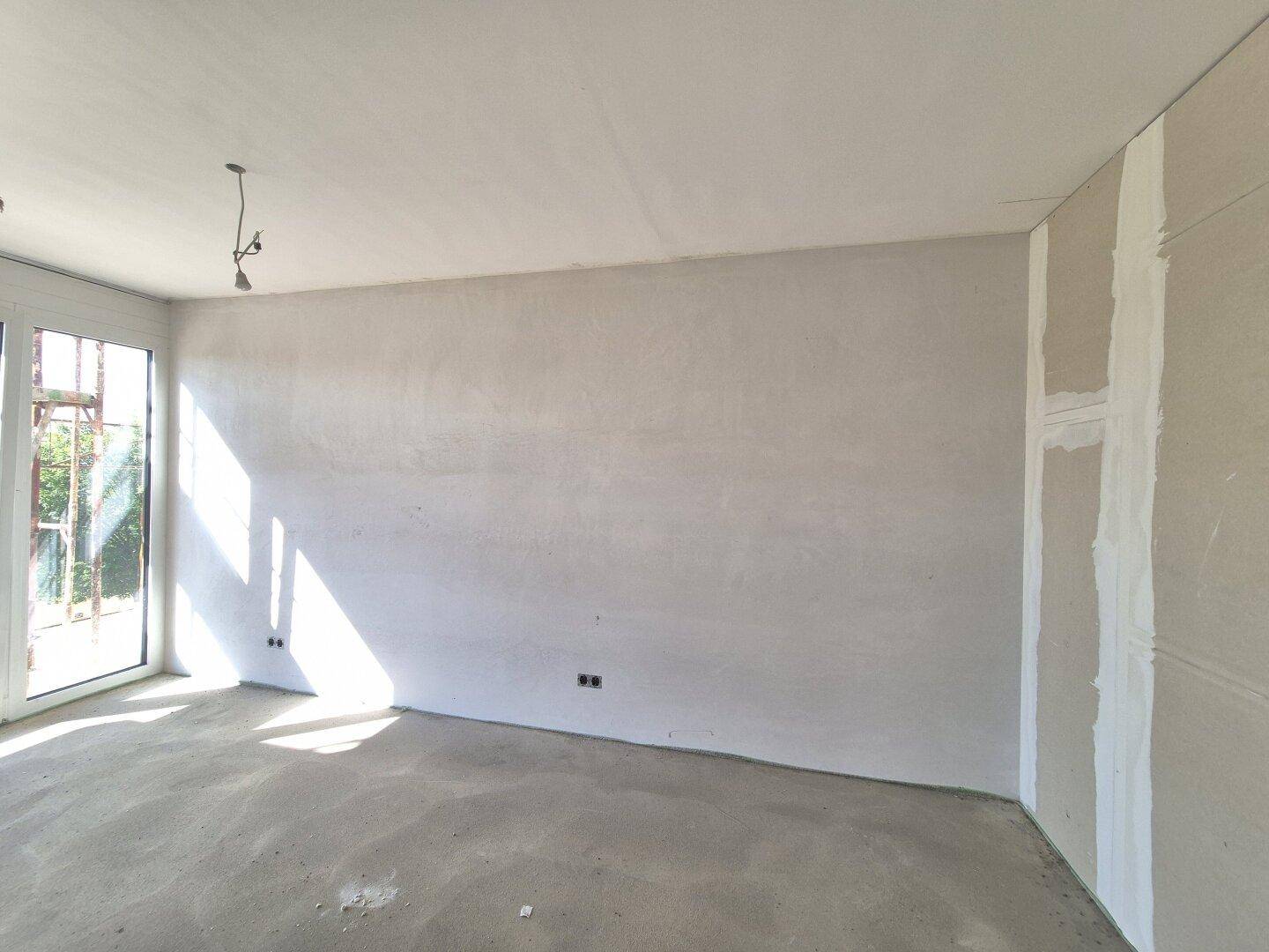 Unfertiger Raum mit großen Fenstern und viel Tageslicht, bereit für den finalen Ausbau.