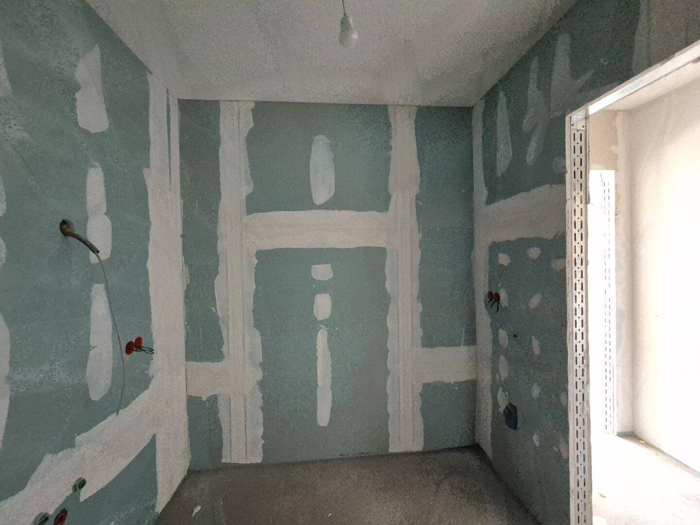 Badezimmer im Rohbau mit grünen Trockenbauwänden und sichtbaren Installationen für die Sanitärausstattung.
