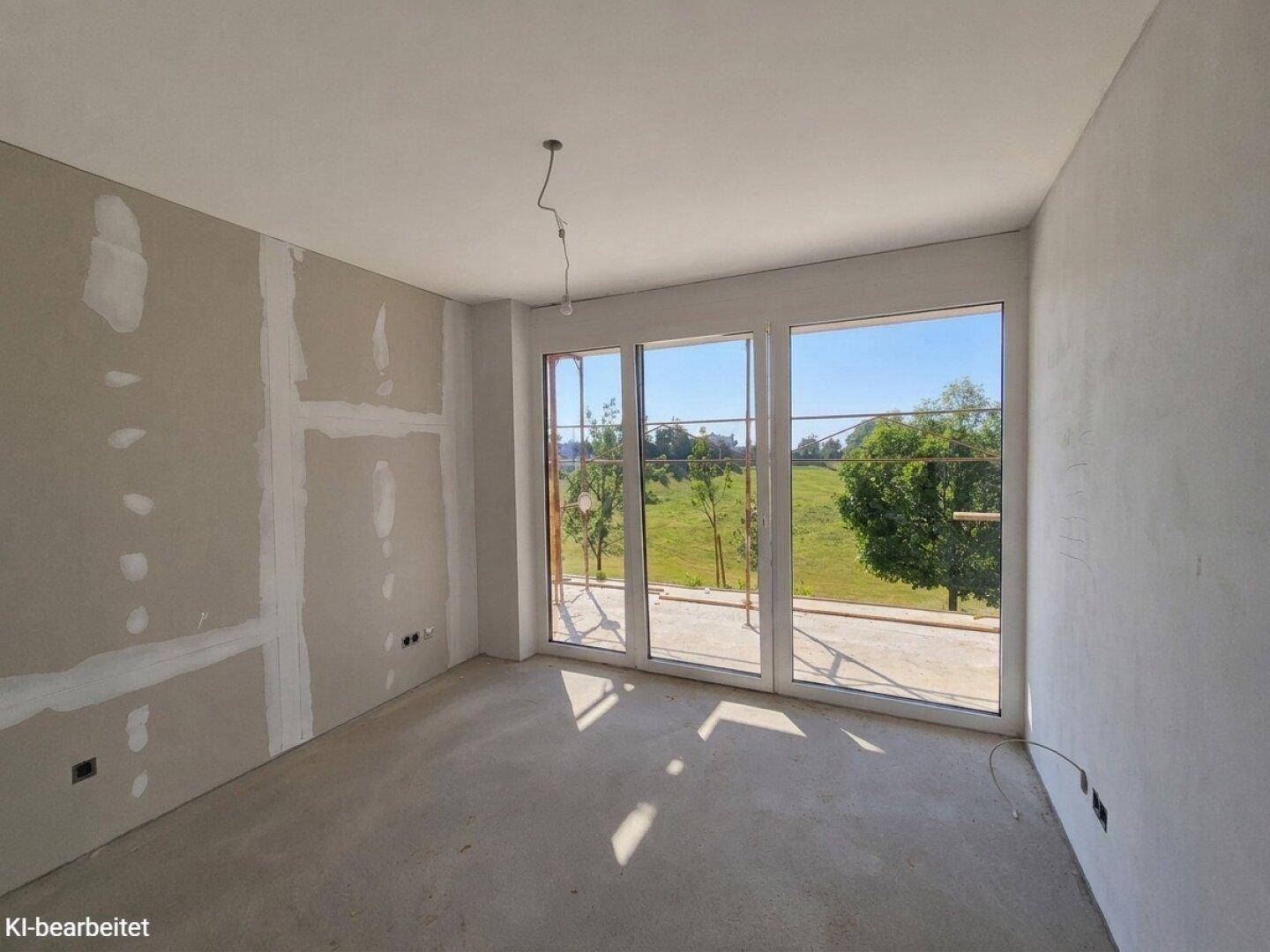 Geräumiger Rohbau mit großen Fenstern, die einen weiten Blick ins Grüne bieten, und Betonboden.