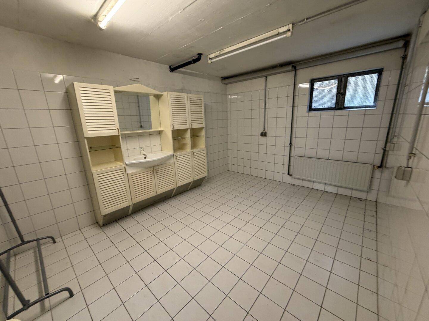 Heller Hauswirtschaftsraum mit gefliesten Wänden, Waschbecken, Spiegelschrank und kleinem Fenster.