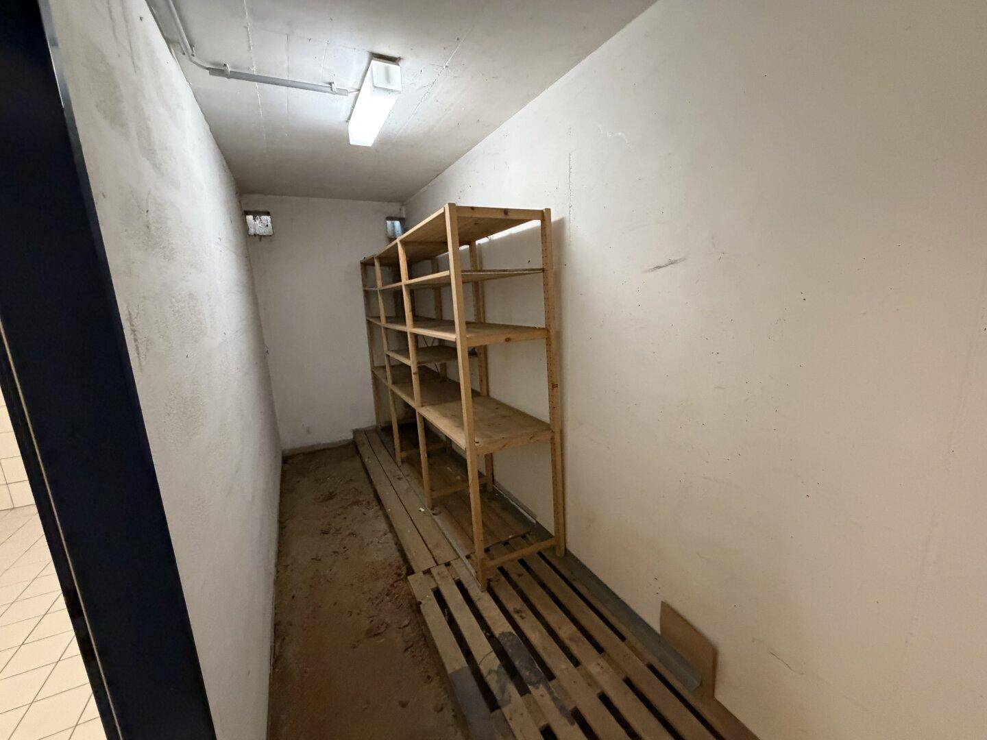 Einfacher Abstellraum mit Holzregalen und unfertigem Boden, ideal für Lagerzwecke im Untergeschoss.