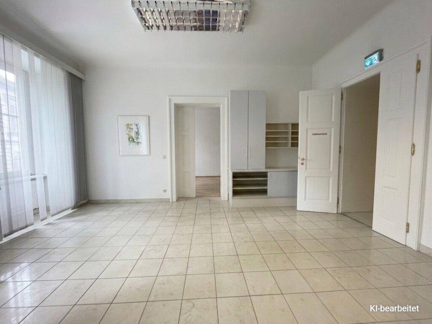 Großer, heller Raum mit Fliesenboden, Deckenleuchten und einem Fenster mit vertikalen Jalousien.