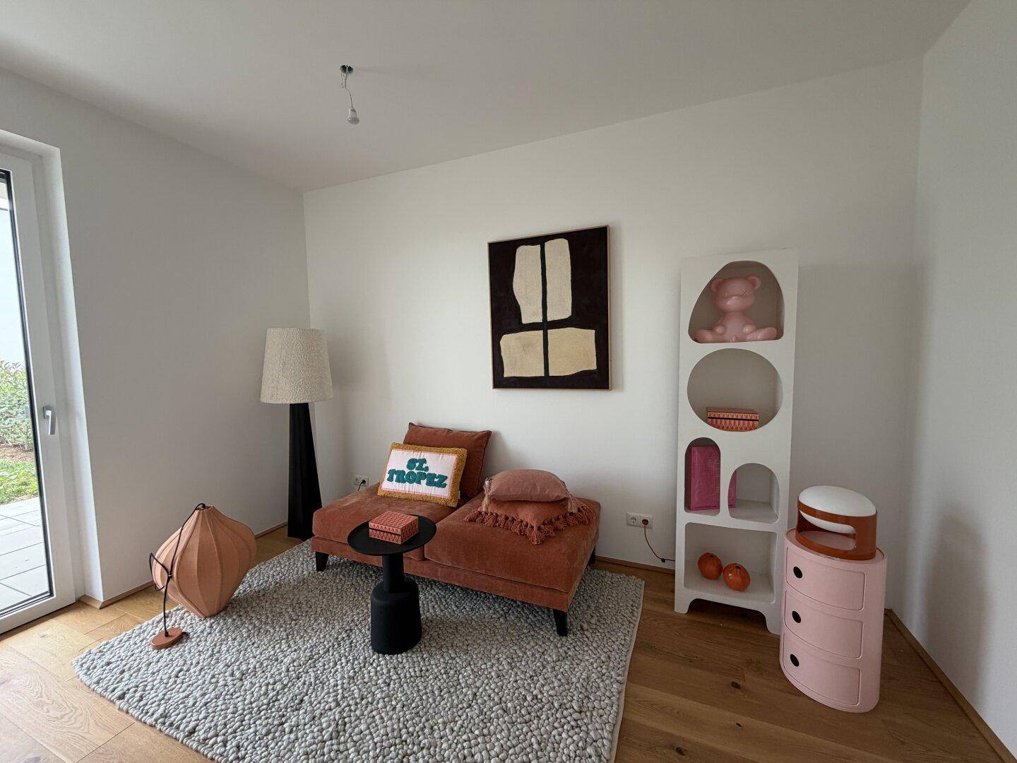 Heller Raum mit orangefarbener Chaiselongue, modernem Regal und Holzboden.