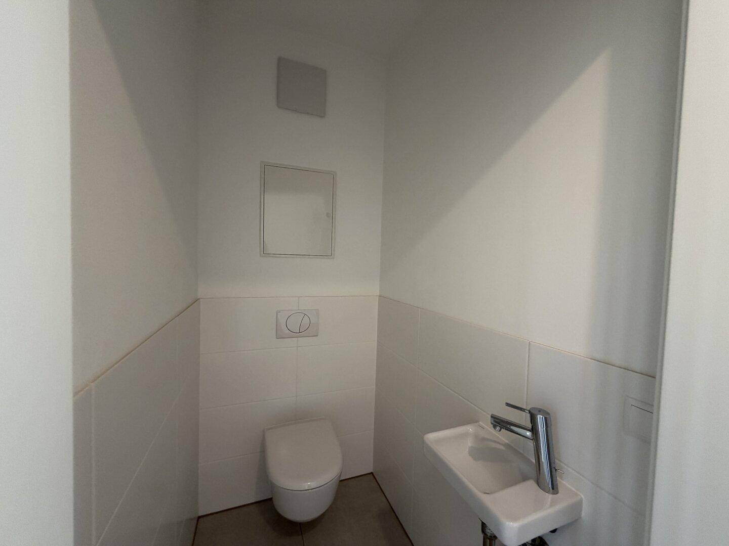 Modernes Gäste-WC mit Wand-WC, kleinem Waschbecken und weißen Fliesen.
