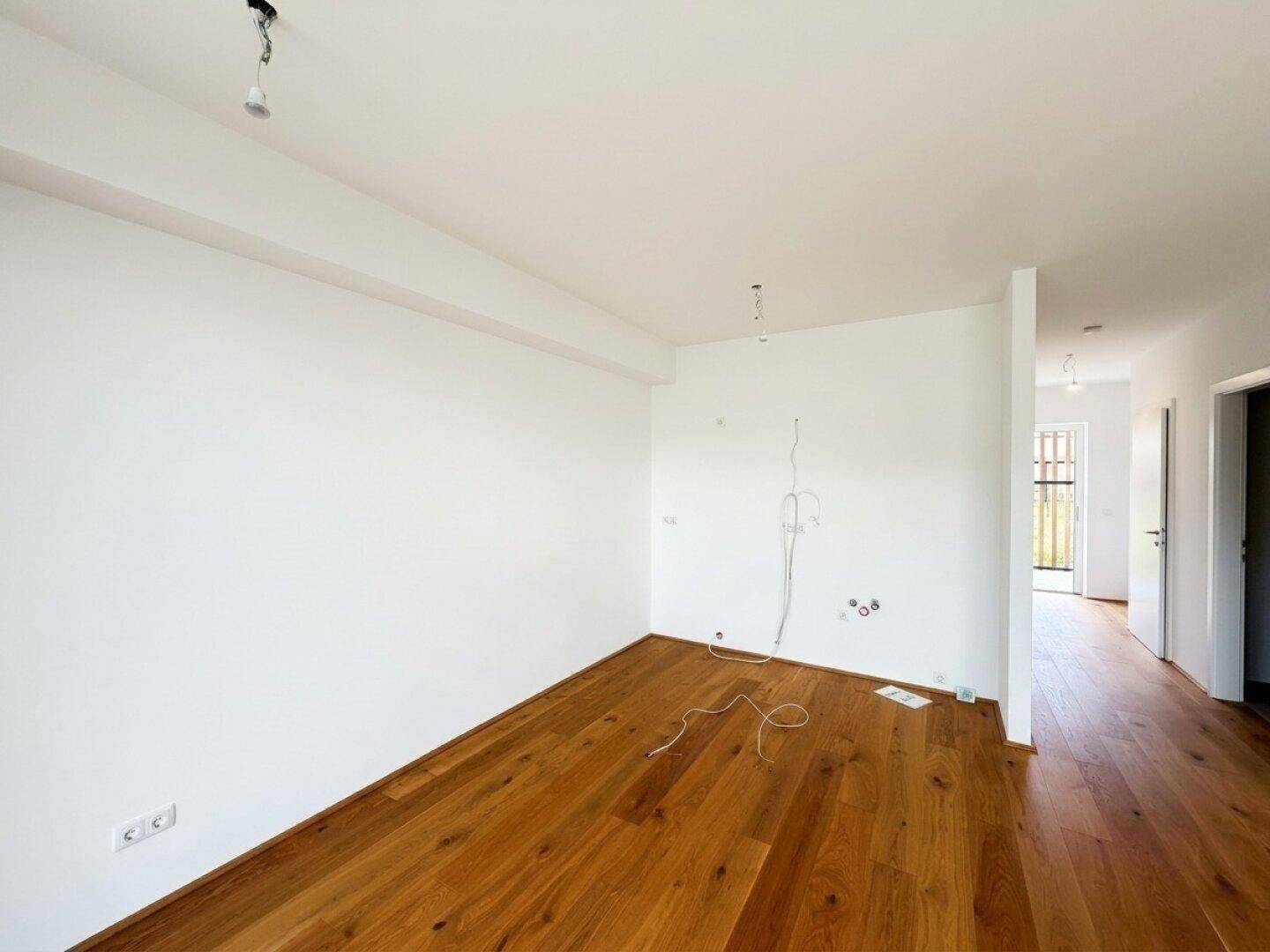 Geräumiger, heller Wohnbereich mit Holzboden und vorbereiteten Anschlüssen für Beleuchtung.