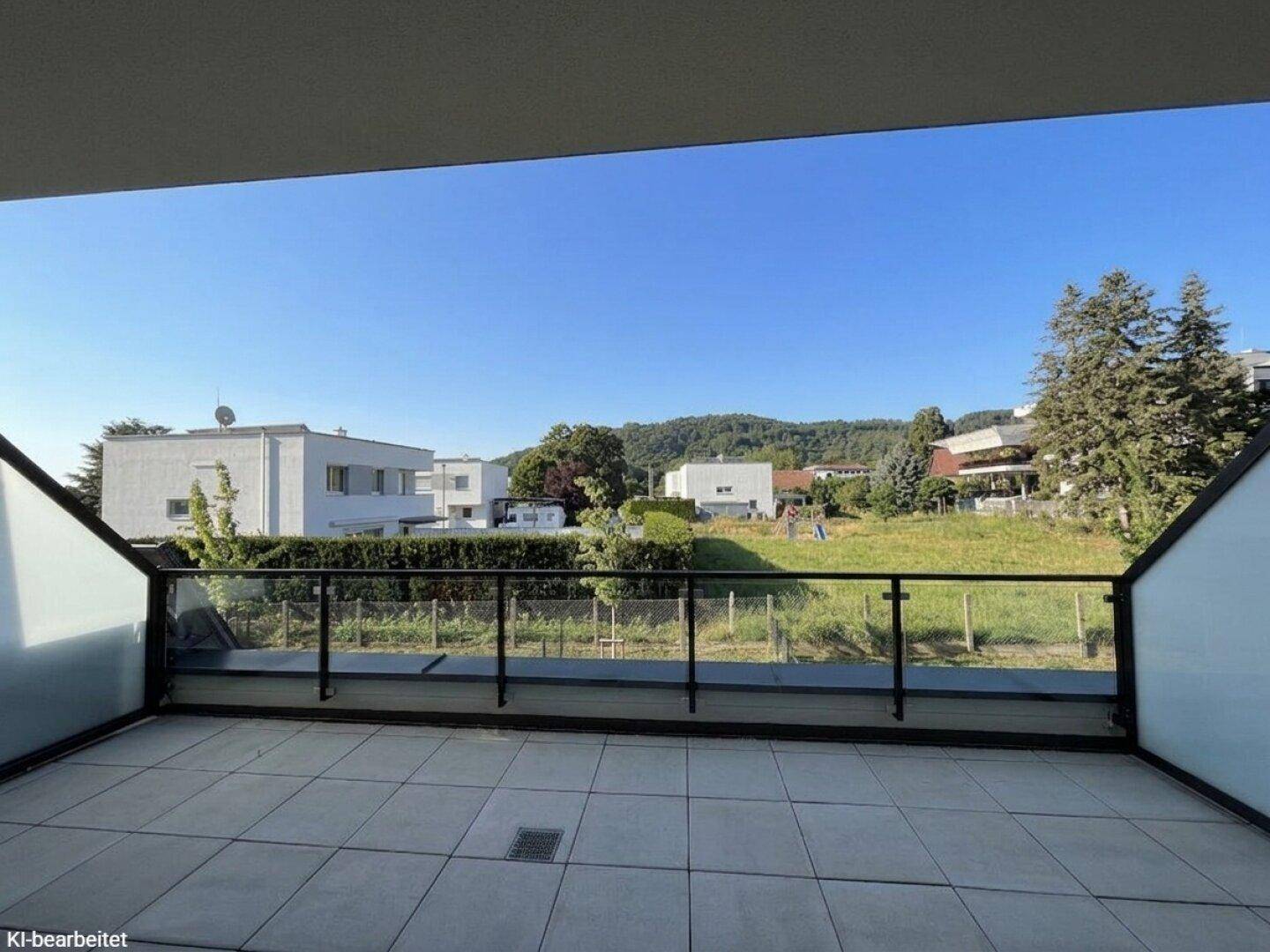 Sonniger Balkon mit Fliesenboden und freiem Blick auf die umliegende Wohngegend und Natur.