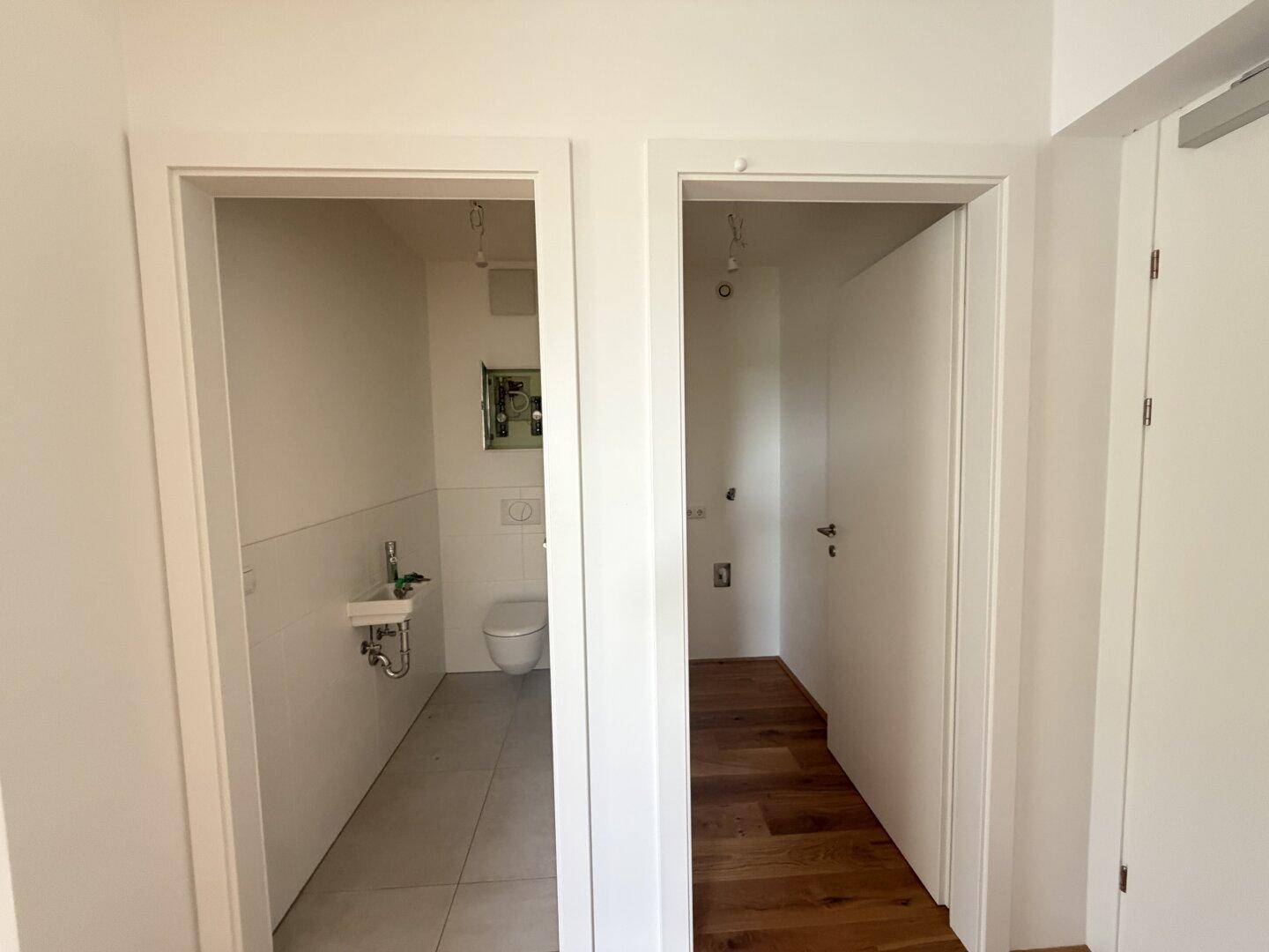 Separates Gäste-WC mit kleinem Waschbecken und Toilette, daneben ein Flur.