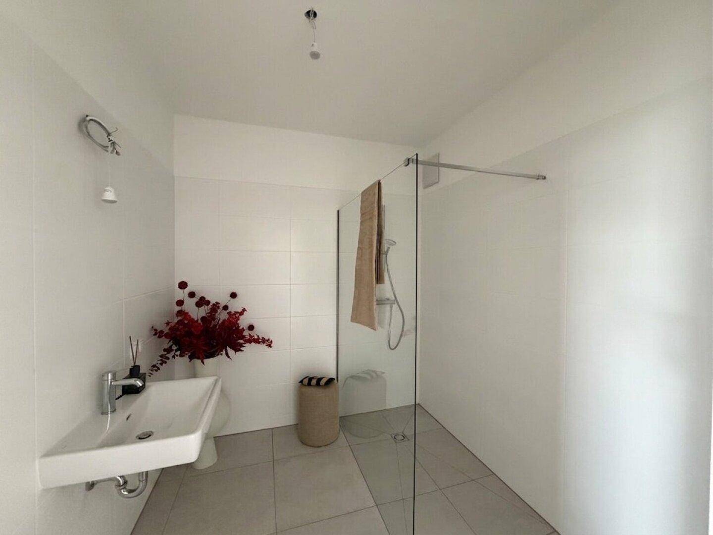 Modernes Badezimmer mit ebenerdiger Dusche, weißem Waschbecken und großen Fliesen, die ein sauberes Ambiente bieten.