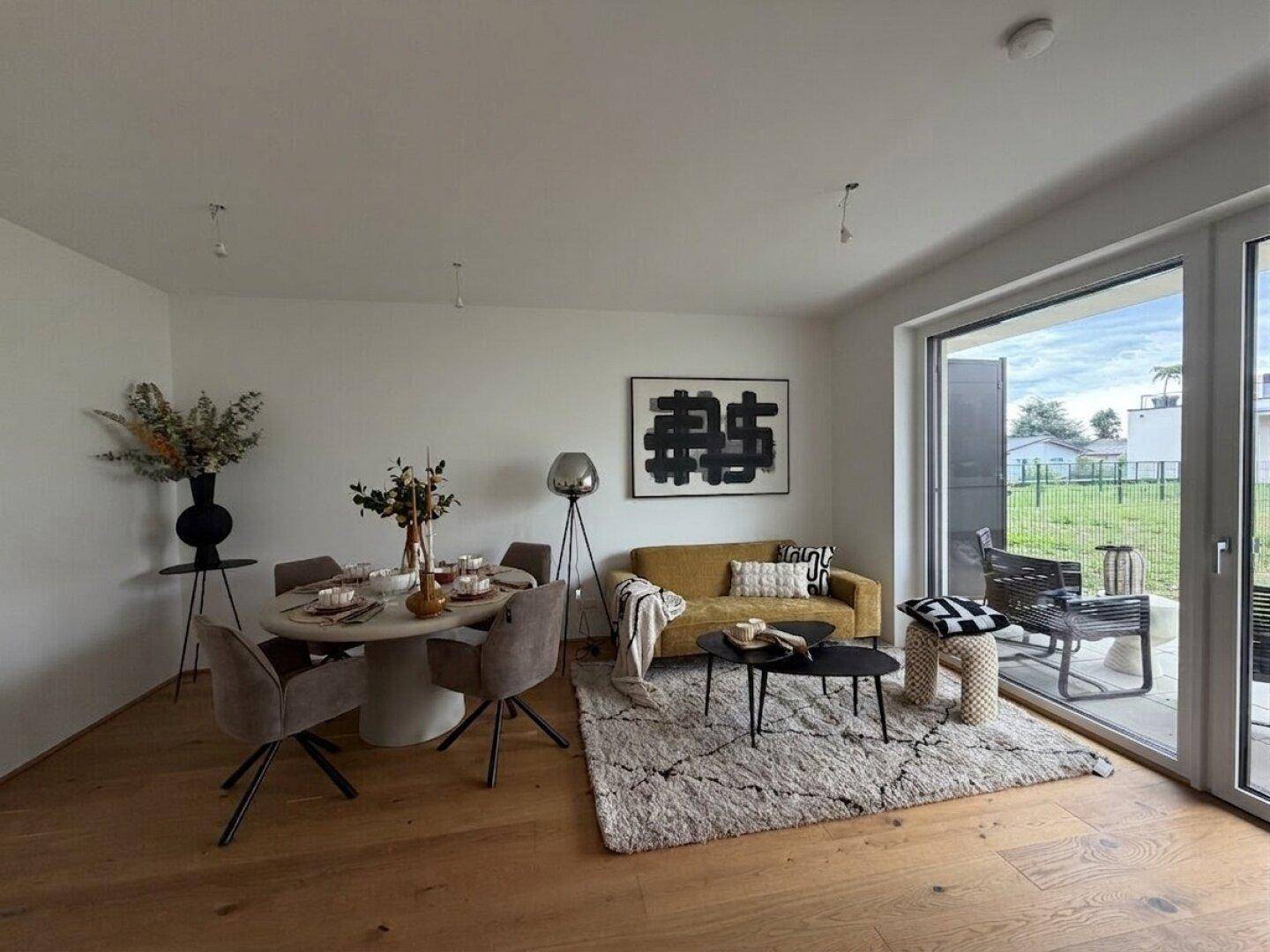 Offener Wohn- und Essbereich mit Holzboden, moderner Einrichtung und großem Fenster mit Zugang zur Terrasse.