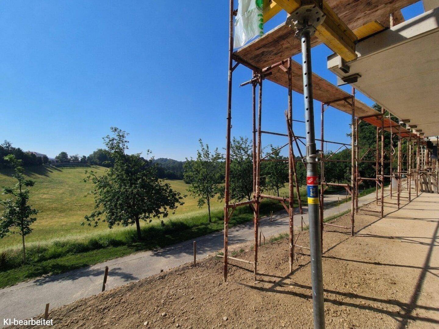 Baustelle mit Gerüst und Rohbau einer Terrasse, die einen weiten Blick über grüne Felder und Bäume bietet.