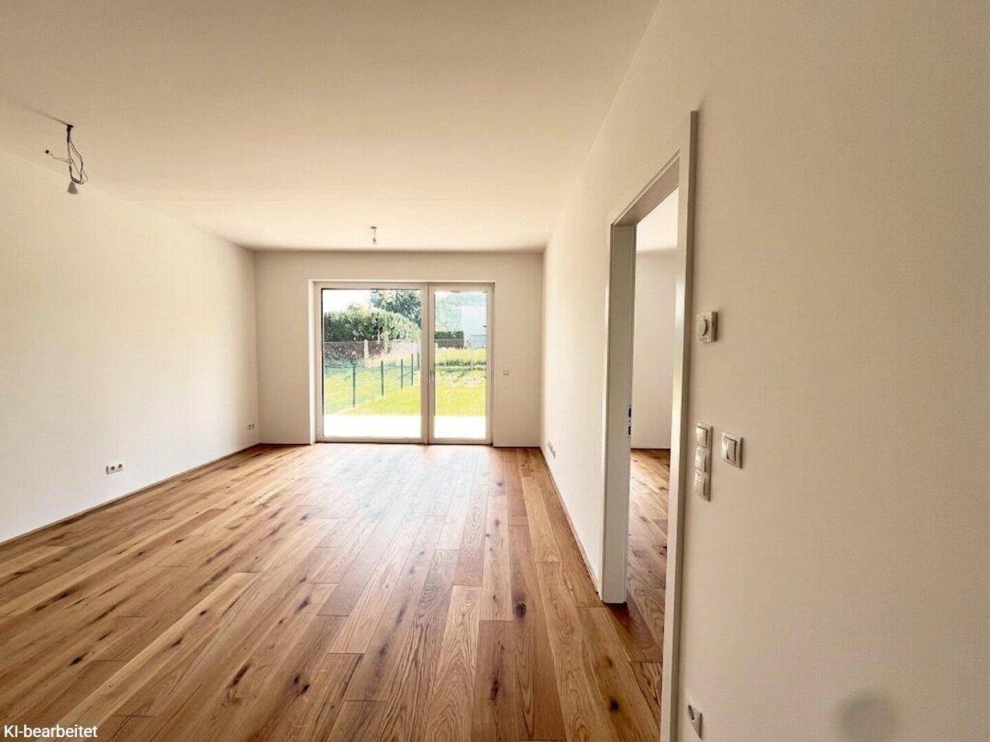 Helles, leeres Wohnzimmer mit hochwertigem Parkettboden und Zugang zum Garten.