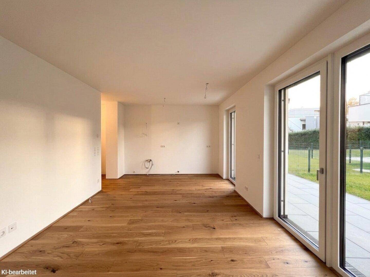 Helles, unmöbliertes Zimmer mit Holzboden und großen Fenstern, die Zugang zum Garten bieten.