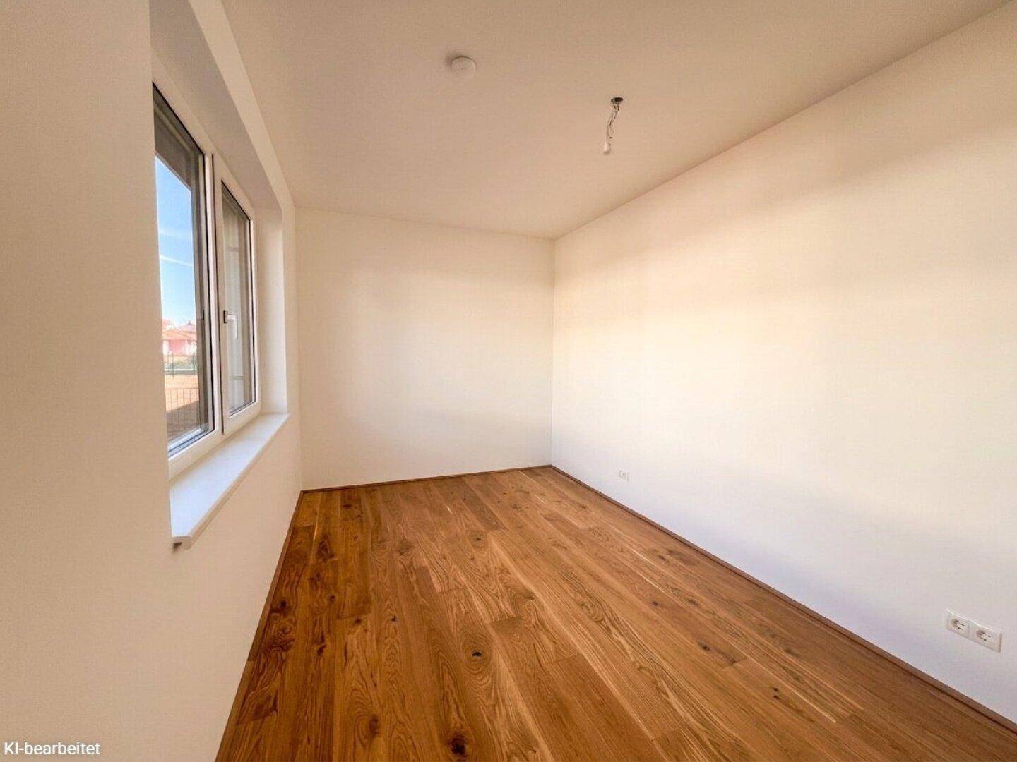 Unmöbliertes Zimmer mit Holzboden und einem großen Fenster, das für viel Helligkeit sorgt.
