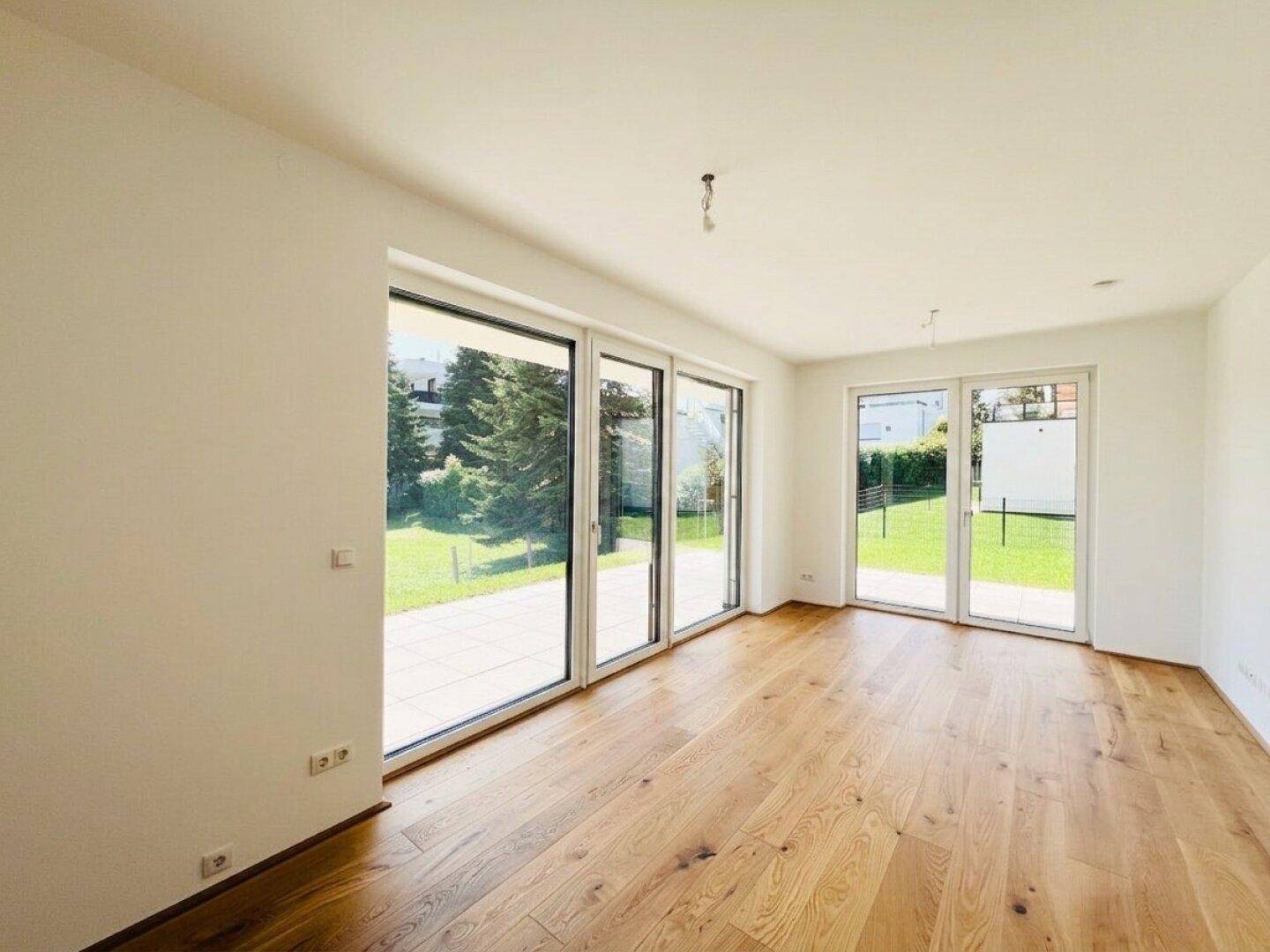 Helles Wohnzimmer mit großen Fenstern, Holzboden und direktem Zugang zum Gartenbereich.