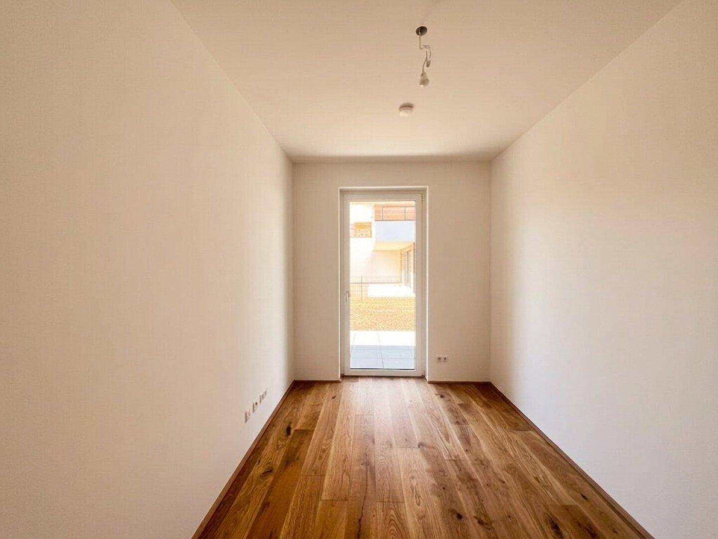 Helles Zimmer mit Holzboden und direktem Zugang zu einem kleinen Außenbereich.