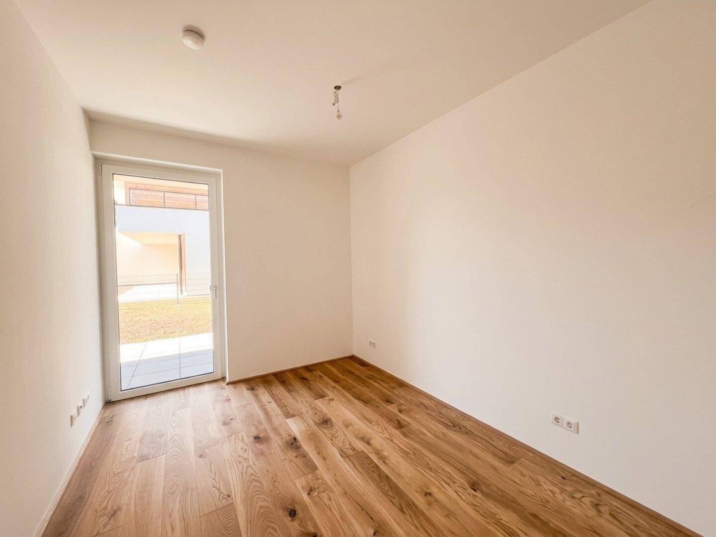 Unmöbliertes Zimmer mit Holzboden und Zugang zu einem kleinen Außenbereich.